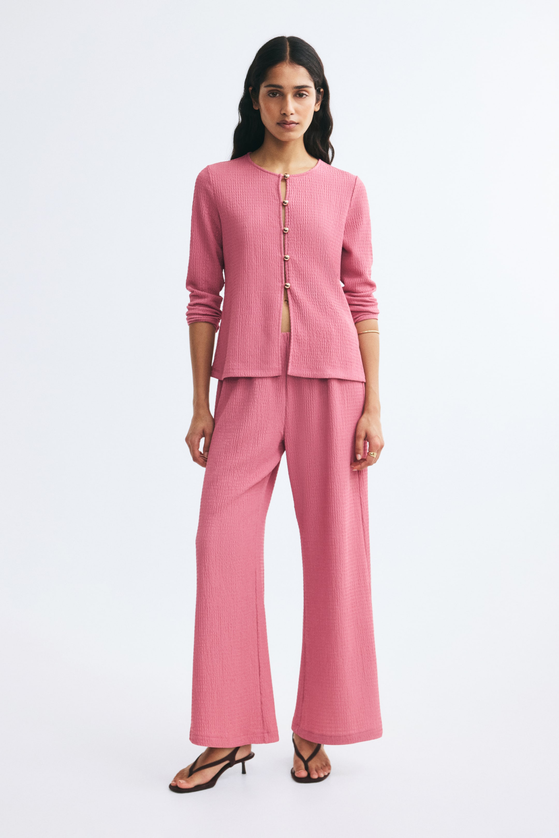 View larger image: Pink textured-jersey pants are shown from a front angle, featuring a relaxed fit with wide, straight legs. The pants are paired with a matching pink textured long-sleeve top that meets at the waist.