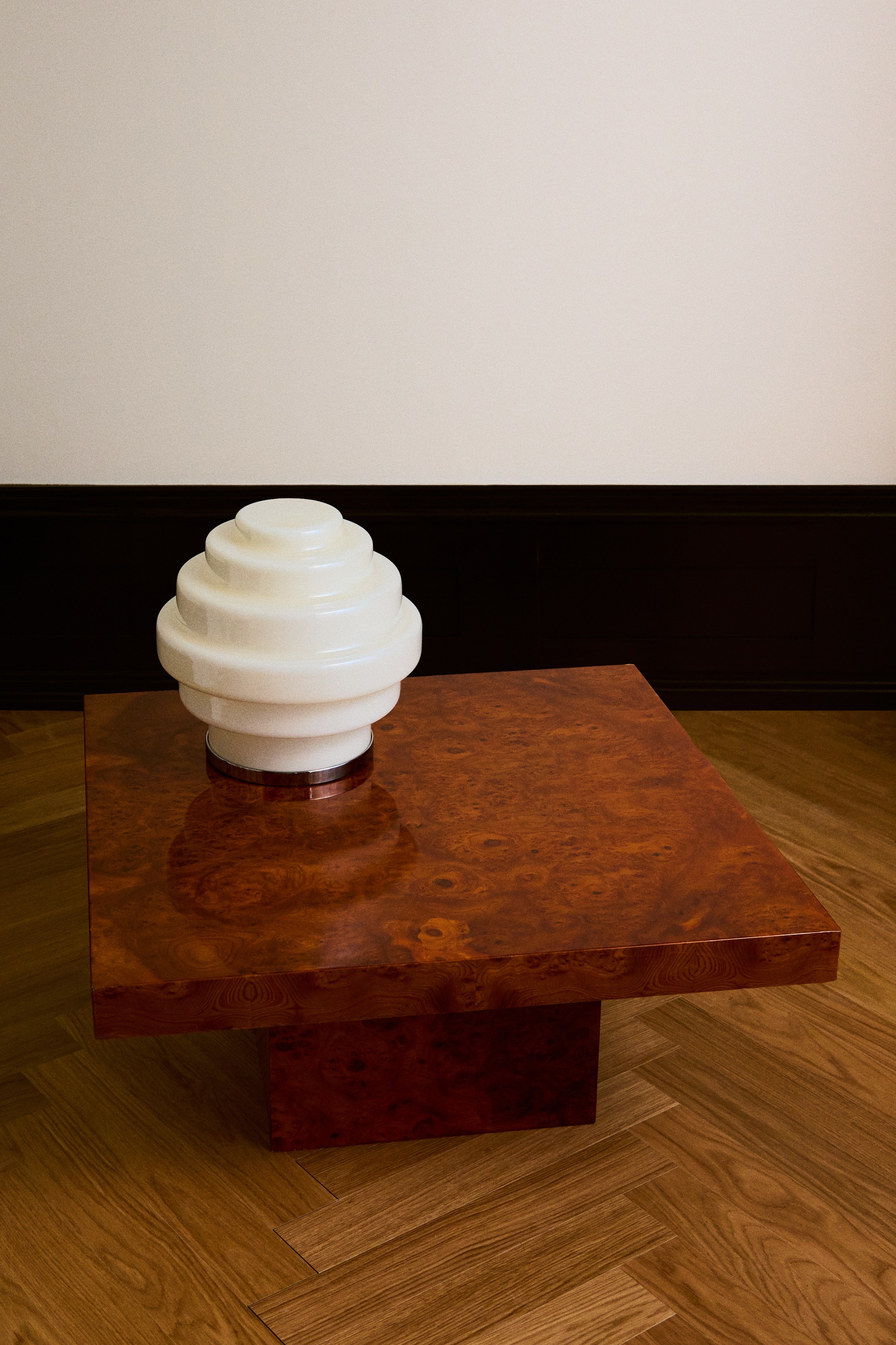 A lamp featuring a tiered, stacked design with five cream-coloured, glossy cylindrical sections, each gradually widening from top to bottom. It rests on a thin, circular silver-toned base, with a braided cord extending from its left side.