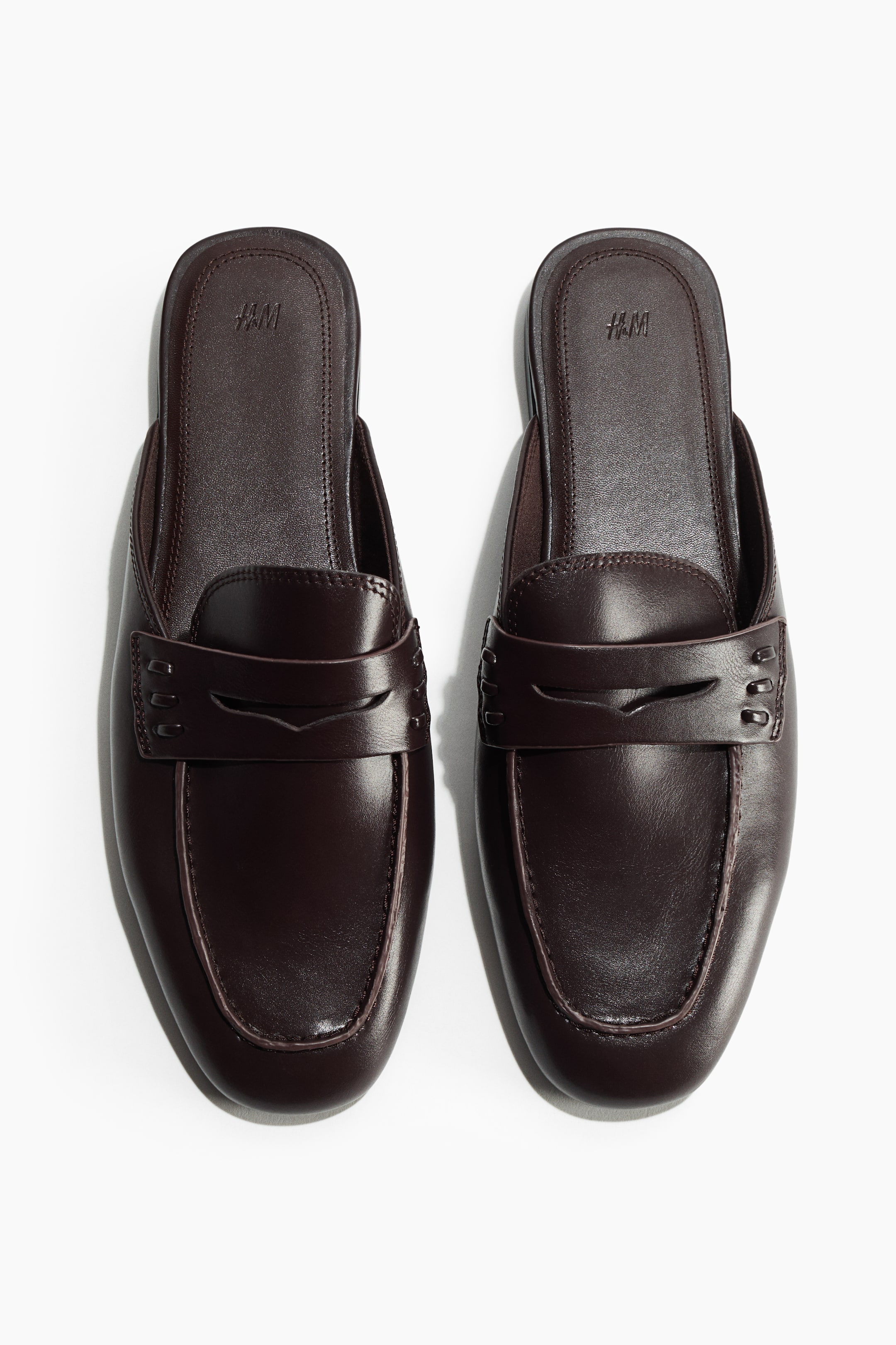 Ver imagen más grande: Mules tipo mocasín en color marrón oscuro con puntera almendrada, detalle de antifaz en la parte superior y costura de mocasín en la parte delantera.