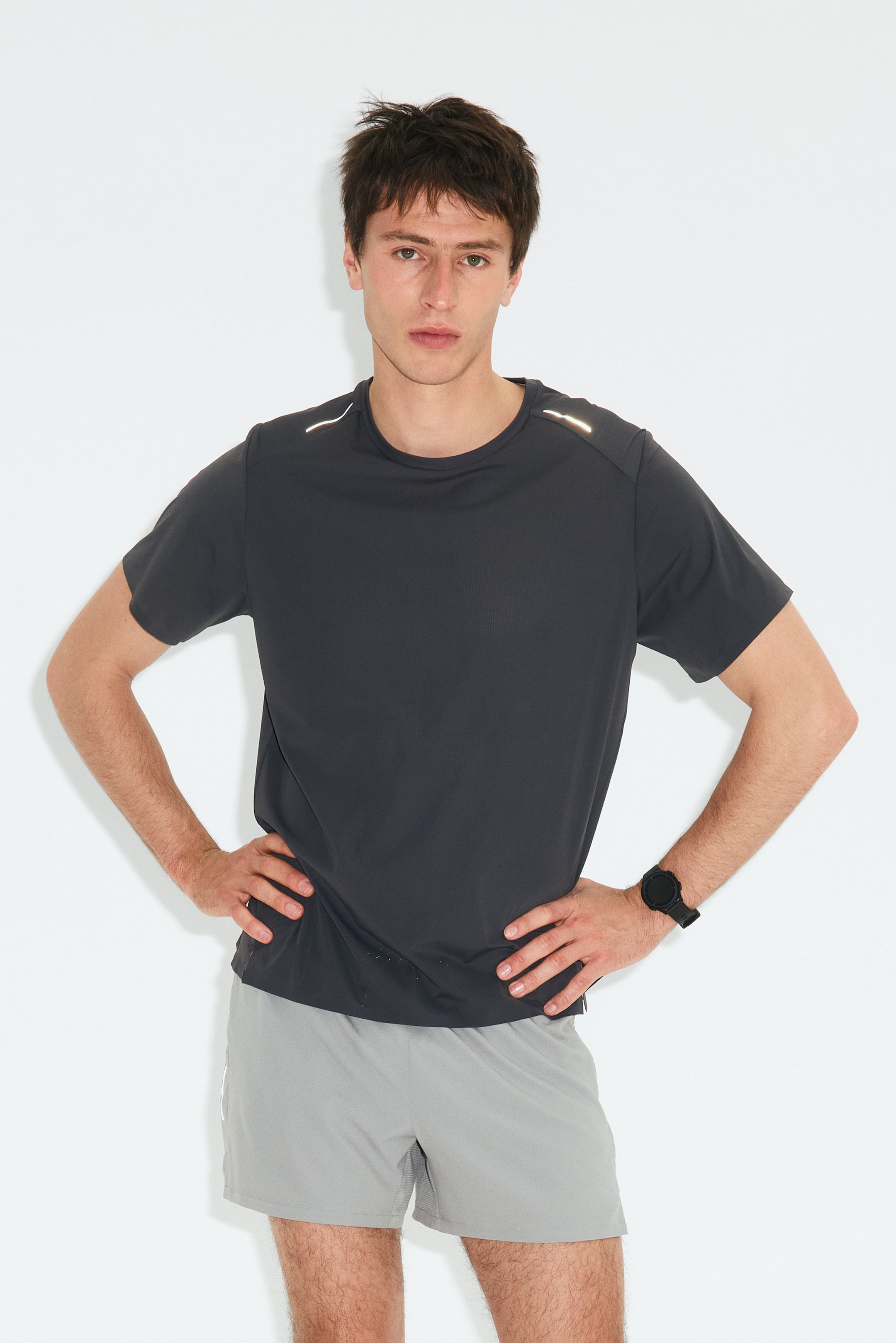 View larger image: The product is a charcoal grey short-sleeved performance t-shirt paired with light grey athletic shorts, displayed facing forward. The t-shirt features a crew neck and reflective strips on the shoulders, while the shorts showcase a subtle vertical stripe along the side.