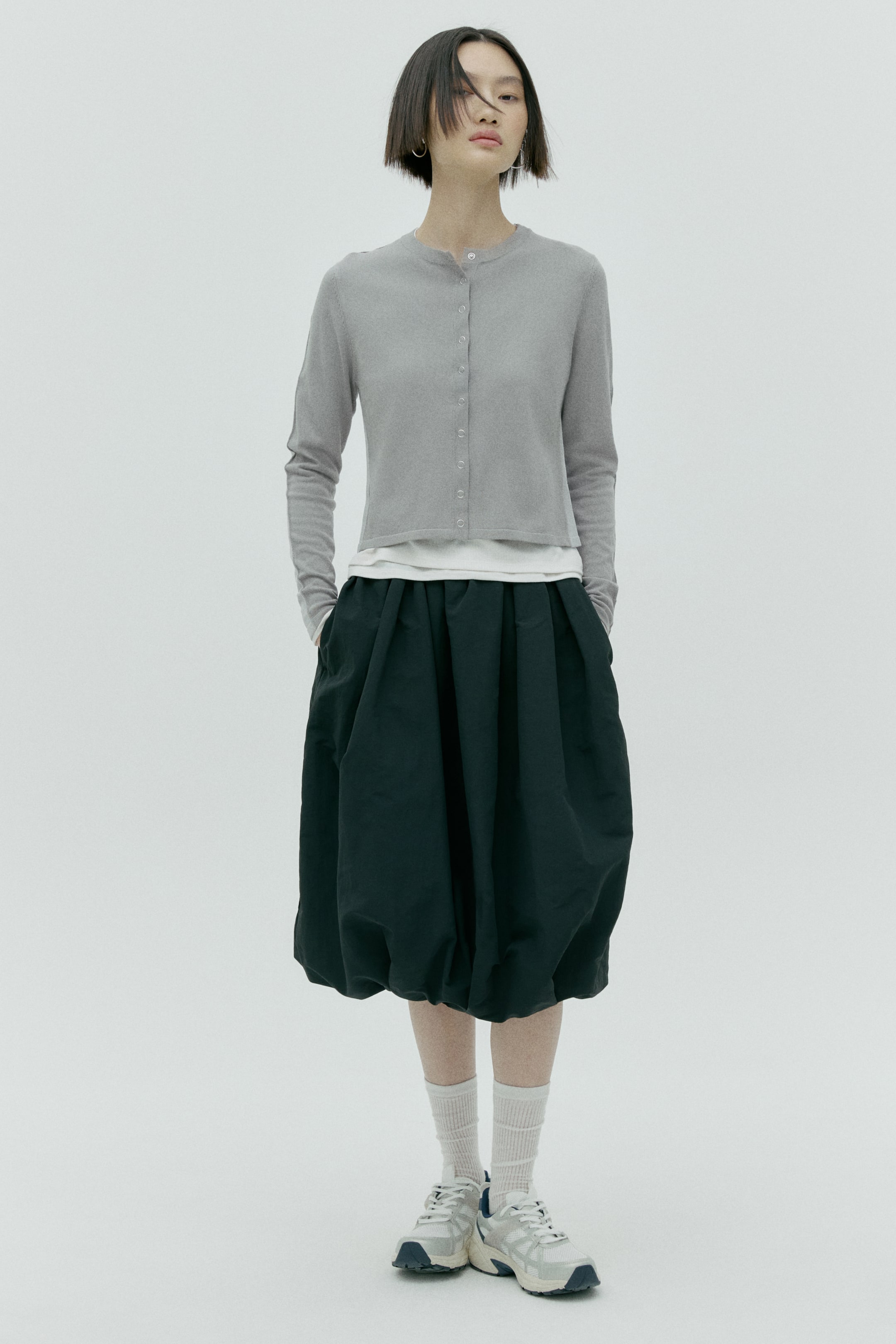 拡大画像を表示: ダークグリーンのバルーンスカートは、ウエストにギャザーを寄せたボリュームのあるシルエットと裾を絞ったデザインが特徴で、膝下までの丈です。ミディ丈のスカートにはサイドポケットが配され、手を入れた状態での着用イメージを見せています。