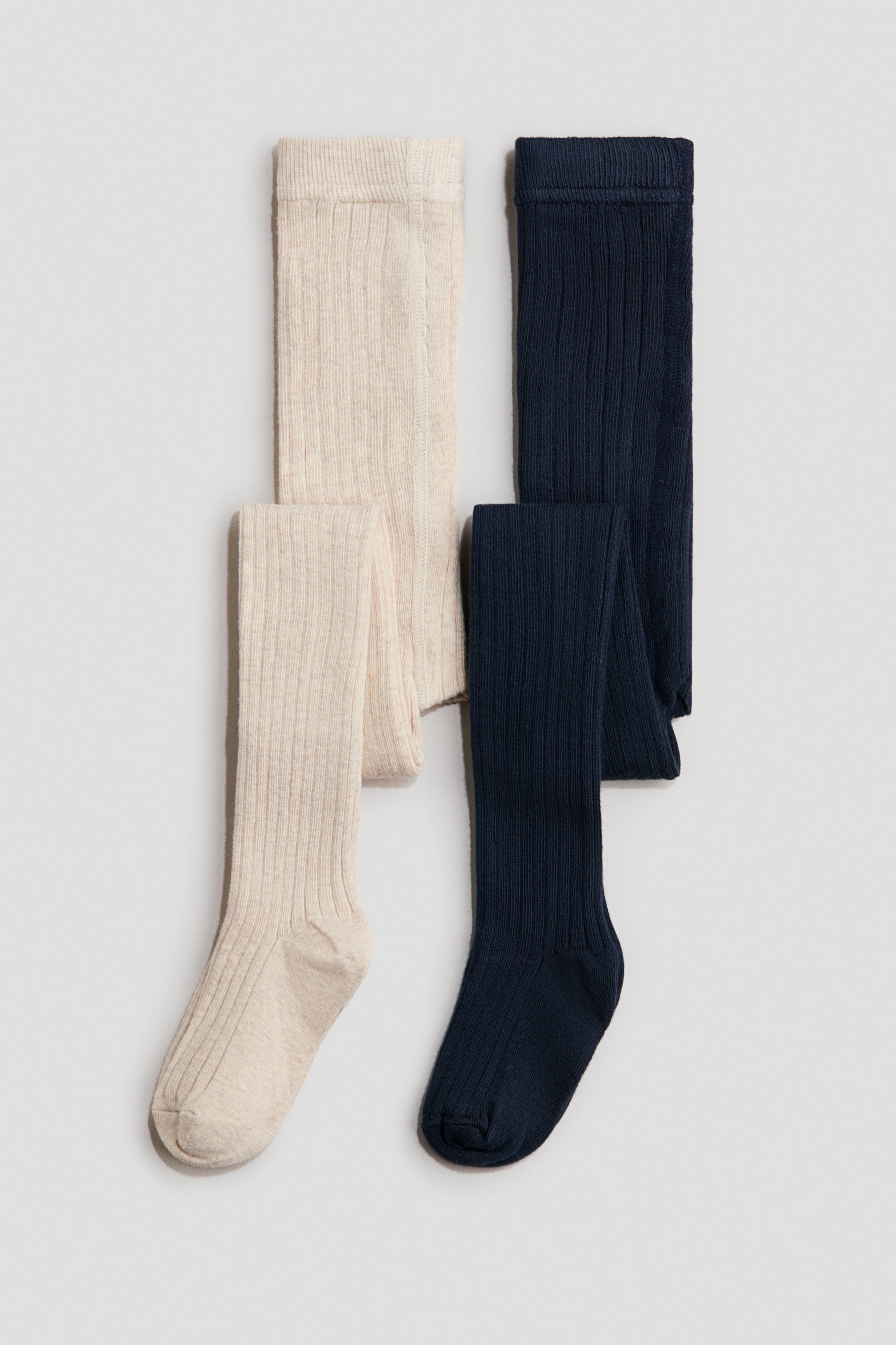 Zobacz większy obraz: H&M Adorables Rajstopy prezentują dwie pary rajstop z prążkowaną dzianiną: jedną w kolorze jasnobeżowym, a drugą w ciemnym granacie. Każda para jest rozłożona na płasko, ukazując drobno prążkowaną fakturę od złożonego pasa do zamkniętej stopy, z widocznym przodem.
