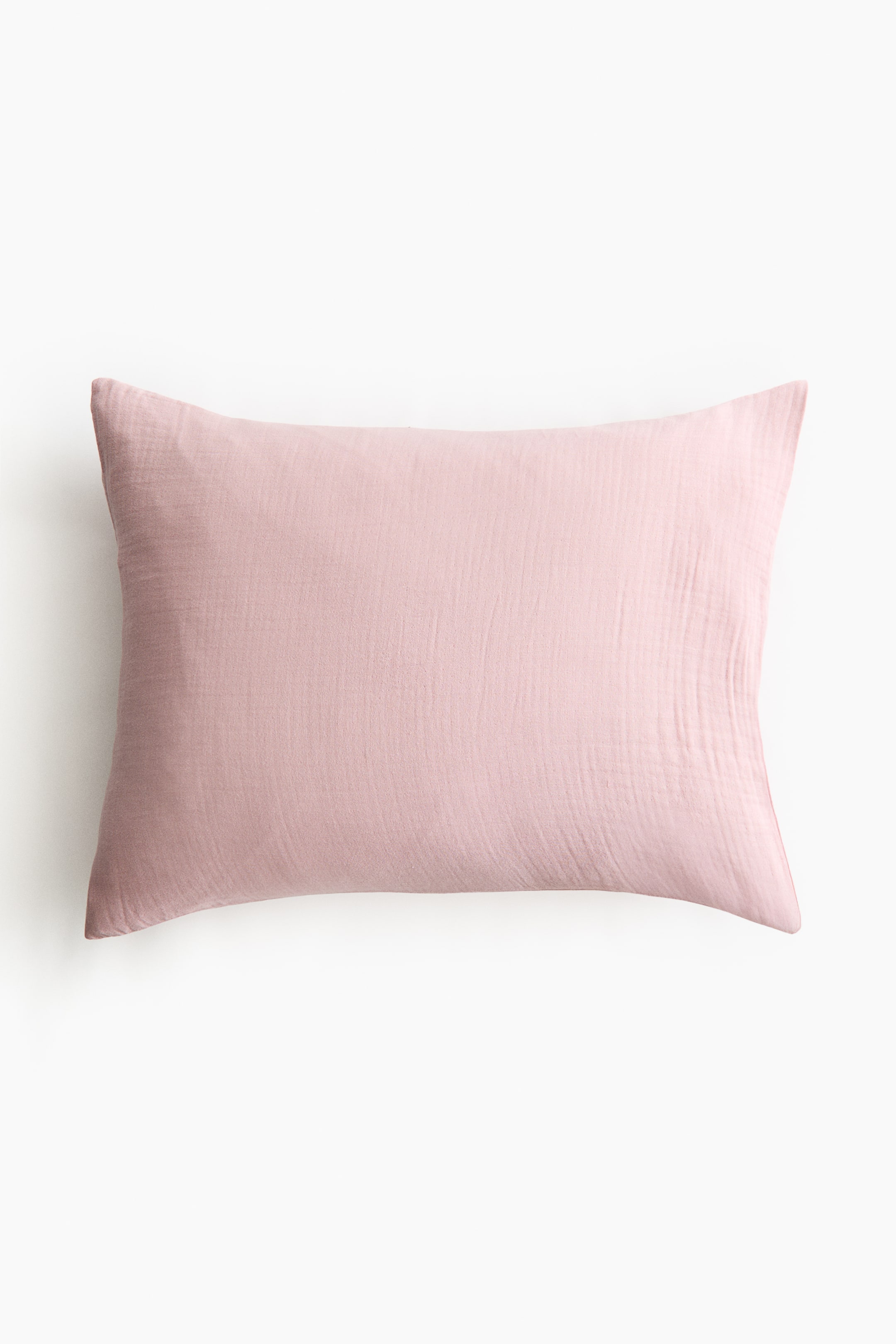 拡大画像を表示: 淡いピンク色の長方形の枕カバーは、柔らかくしわのあるコットンモスリンの質感を見せています。視聴者に向かって前面が見えるように、詰め物が入っているように見えます。