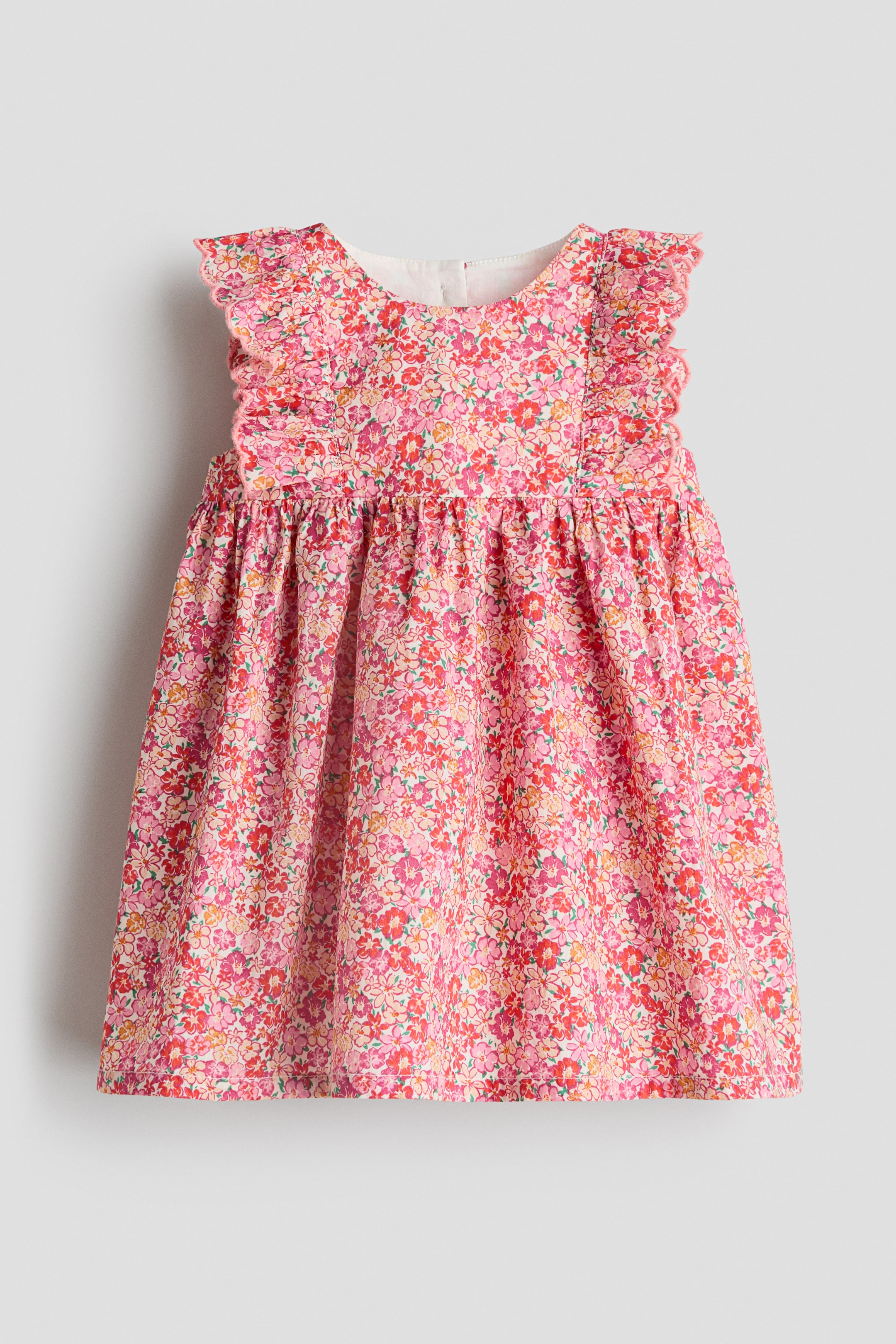 View larger image: A front-facing pink floral dress showcasing a round neckline and ruffled shoulder straps with picot edging. The dress boasts a gathered waistline and a full skirt, adorned with a small floral pattern in shades of pink, red, and orange.