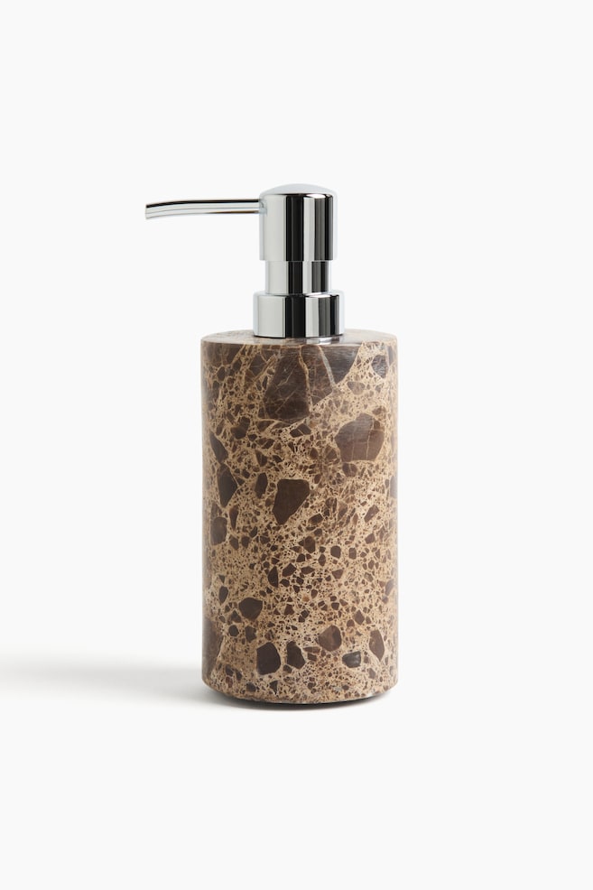 A cylindrical soap dispenser featuring a brown marble body with diverse earthy hues and lighter speckled patterns. A glossy chrome pump mechanism tops it off, with its spout extending horizontally forward. - 1
