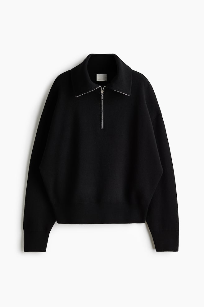 A black knit half-zip sweater is facing front, displaying a relaxed fit with dropped shoulders and long sleeves ending in ribbed cuffs. The sweater is featuring a spread collar with a silver-toned half-zip closure and a wide ribbed hem. - 1
