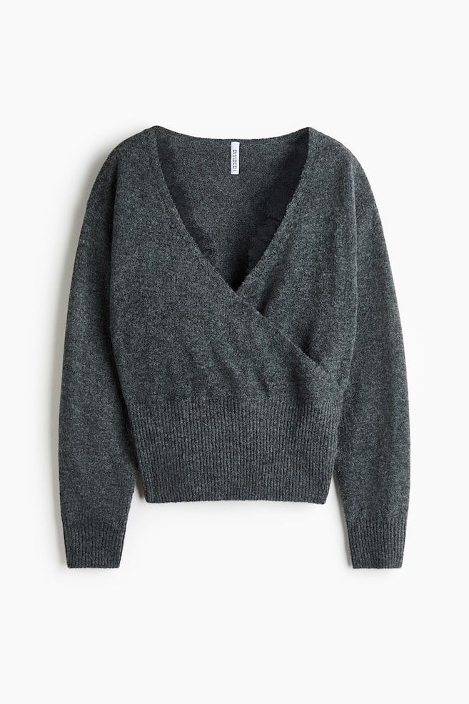 Ein dunkelgrau melierter Strickpullover ist von vorne zu sehen und prÃ¤sentiert ein Wickeldesign, das einen tiefen V-Ausschnitt mit schwarzer Spitzenborte entlang der inneren Kante erzeugt. Der Pullover zeigt lange Ãrmel mit RippbÃ¼ndchen und einen breiten Rippbund am Saum. - 1