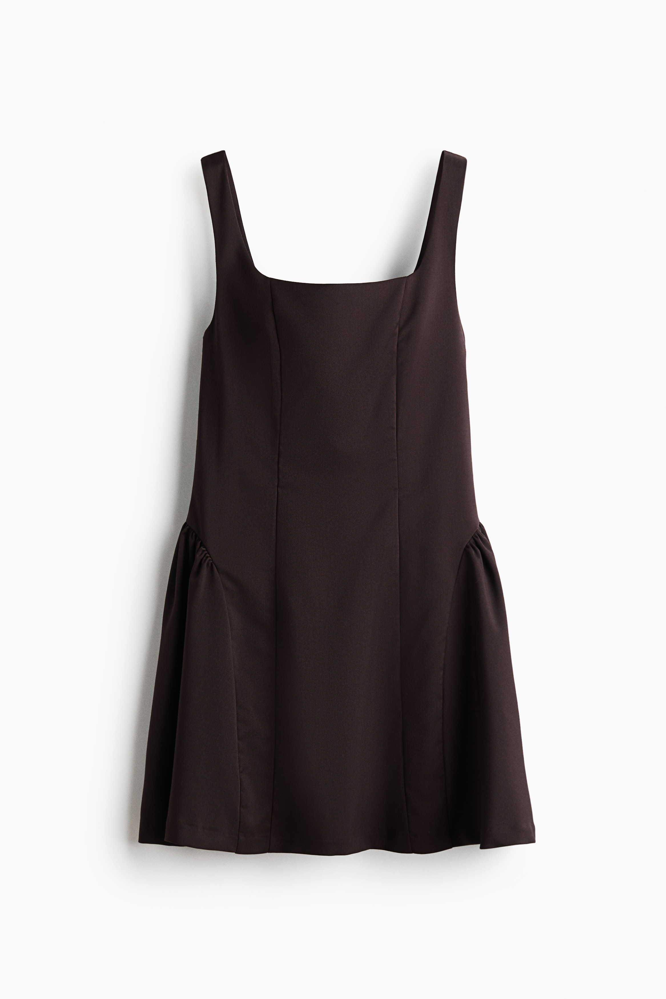 The model is wearing a short dark brown dress featuring a square neckline, wide shoulder straps, a fitted bodice, and a flared skirt with gathered inset panels at the hips. The dress is styled with dark brown lace-up sneakers.