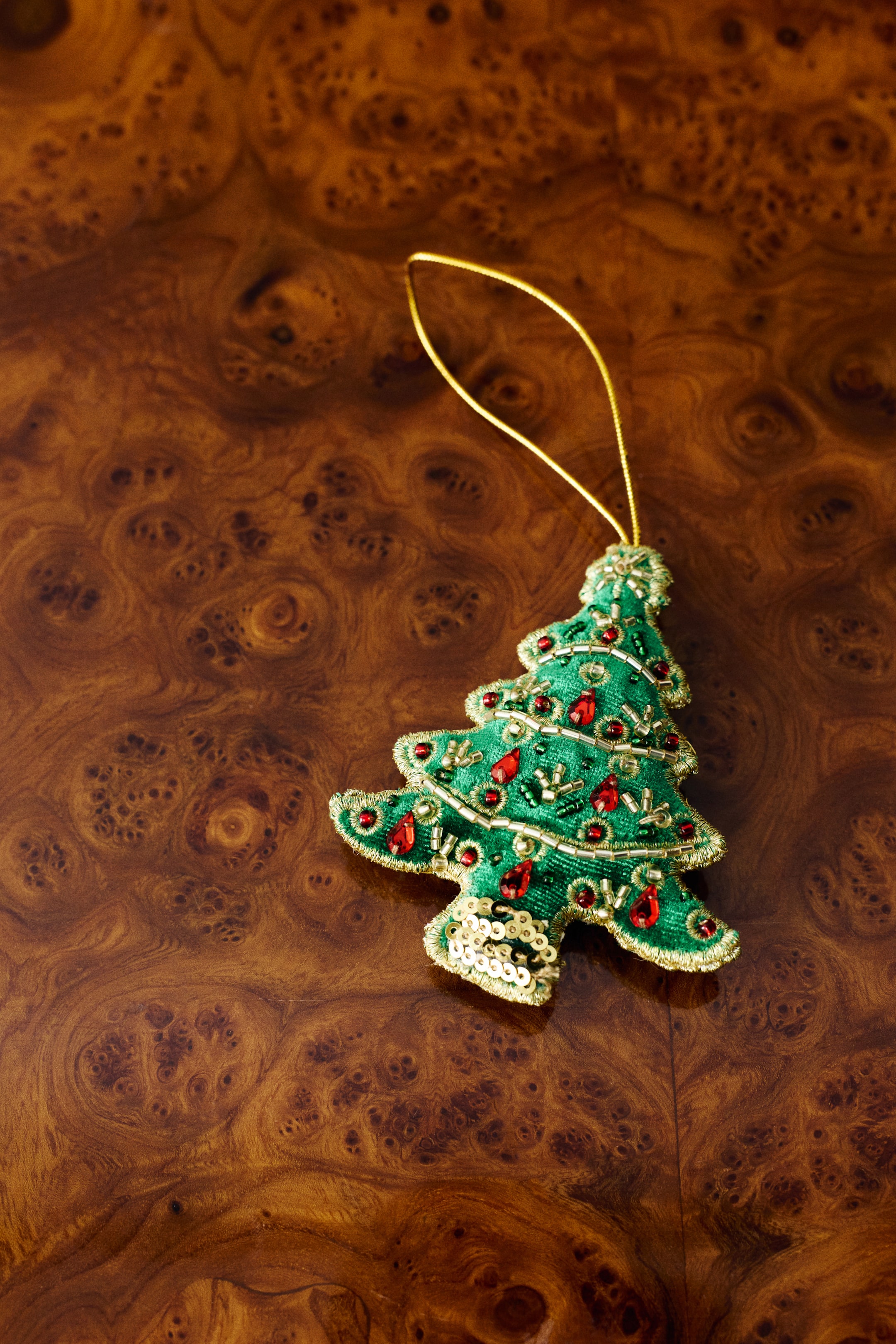 Visualizza l'immagine ingrandita: Un ornamento per albero di Natale in velluto verde mette in risalto decorazioni dettagliate, tra cui gemme rosse a goccia, piccole perline dorate e paillettes dorate sul tronco. Un sottile cordoncino metallico dorato esce dalla parte superiore dell’ornamento per appenderlo.