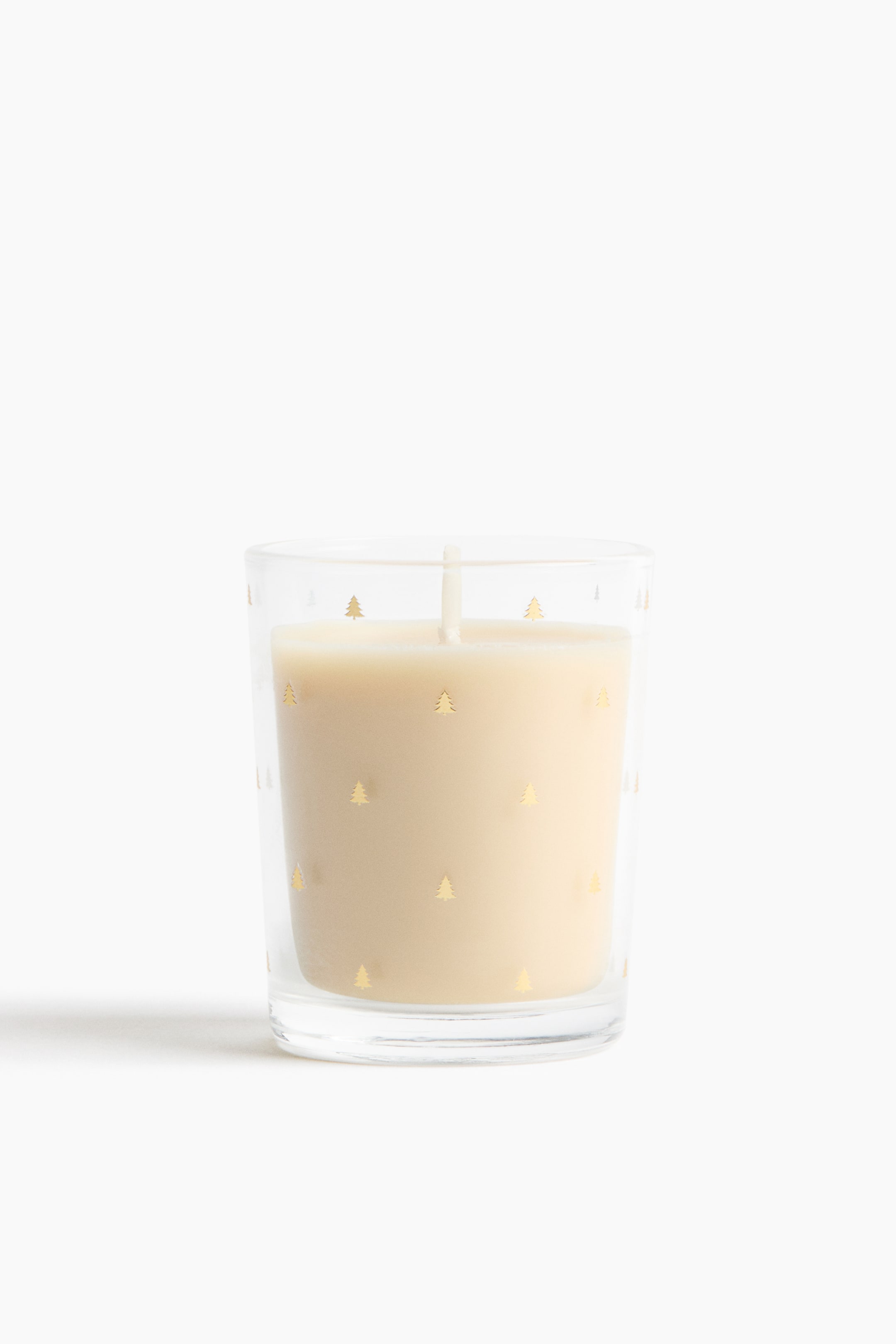 View larger image: A candle in a clear glass vessel is standing upright, showing cream-coloured wax and a single central wick from a front angle. The glass features a repeating pattern of small, metallic gold pine trees.