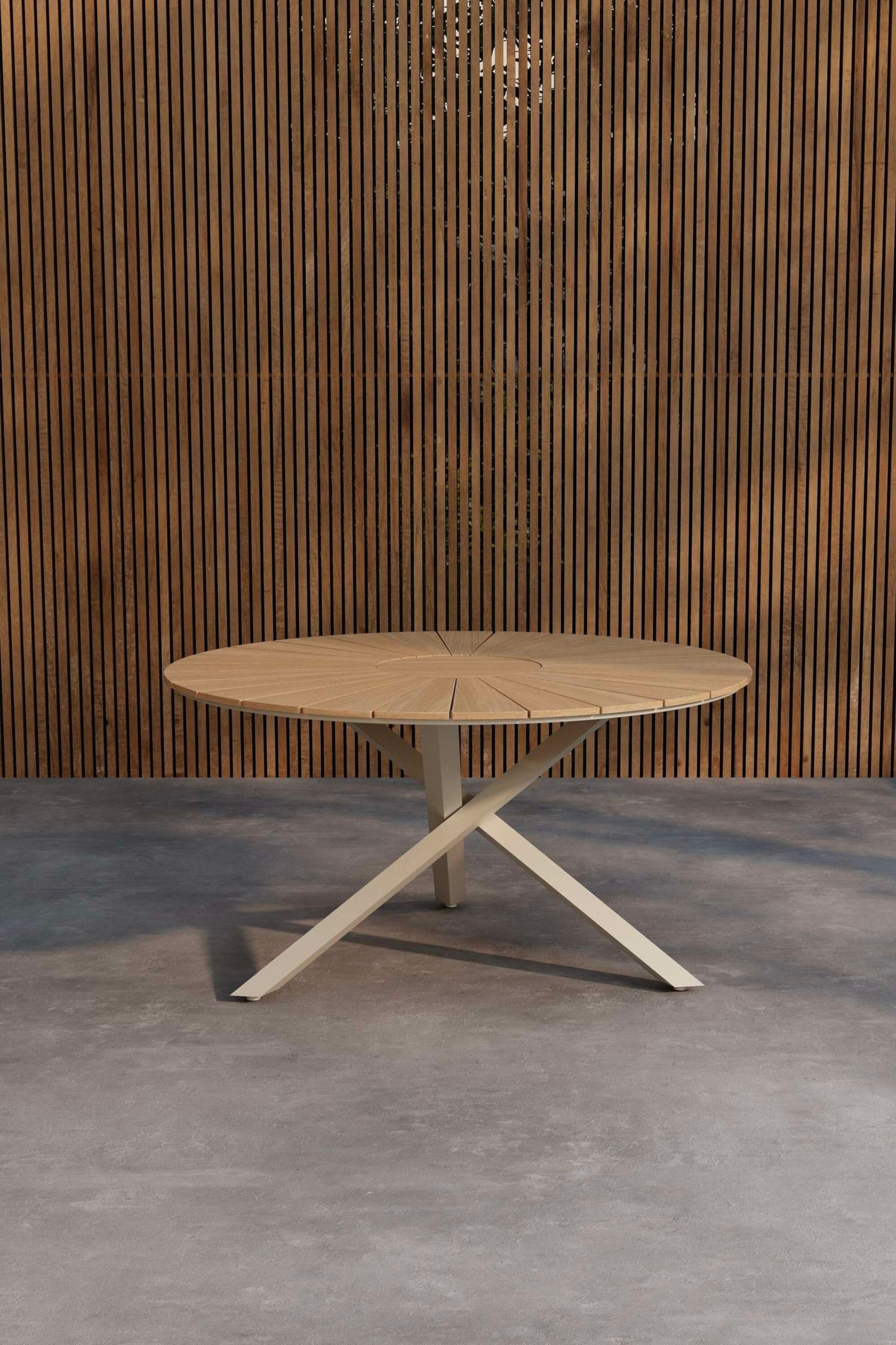 Visualizza immagine più grande: Un tavolo da pranzo rotondo presenta un piano in legno chiaro con listelli che si irradiano da un punto centrale. È posizionato su una base a forma di X di colore crema, visto da un'angolazione frontale leggermente elevata.