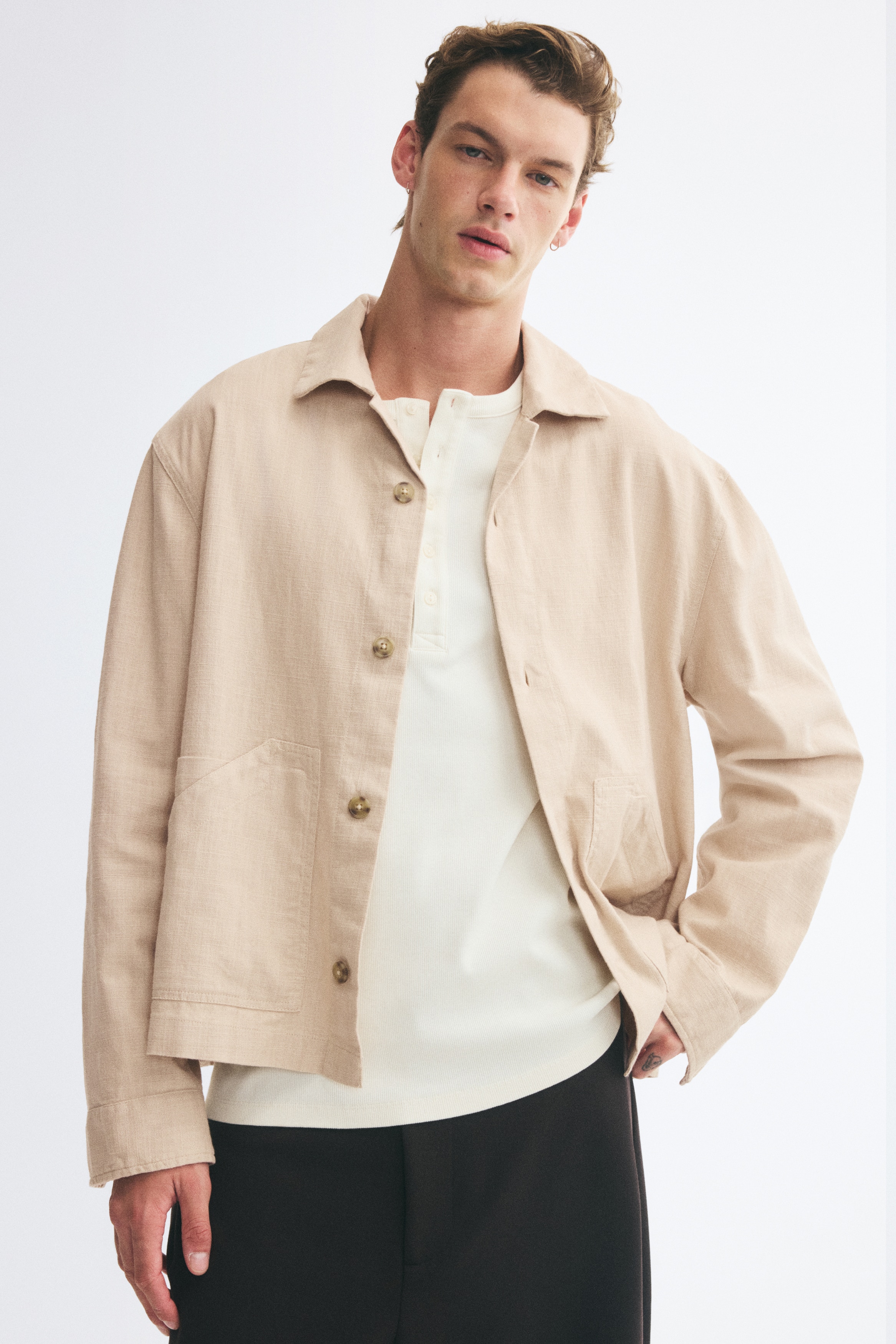 Má»t chiáº¿c Ã¡o khoÃ¡c mÃ u be nháº¡t, cÃ³ bá» máº·t váº£i linen, ÄÆ°á»£c chá»¥p tá»« phÃ­a trÆ°á»c, vá»i cá» Ã¡o camp collar, pháº§n cÃ i bá»n nÃºt vÃ  tay dÃ i. Hai tÃºi há»p lá»n vá»i miá»ng tÃºi chÃ©o ÄÆ°á»£c Äáº·t á» pháº§n thÃ¢n trÆ°á»c phÃ­a dÆ°á»i cá»§a thiáº¿t káº¿ dÃ¡ng tháº³ng, bo gáº¥u.