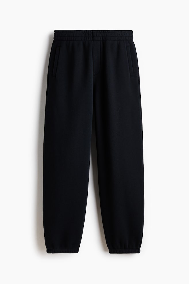 Black sweatpants are presenting a front view, featuring an elastic waistband and two vertical side pockets. The legs are tapering down to elastic cuffs at the ankles. - 1