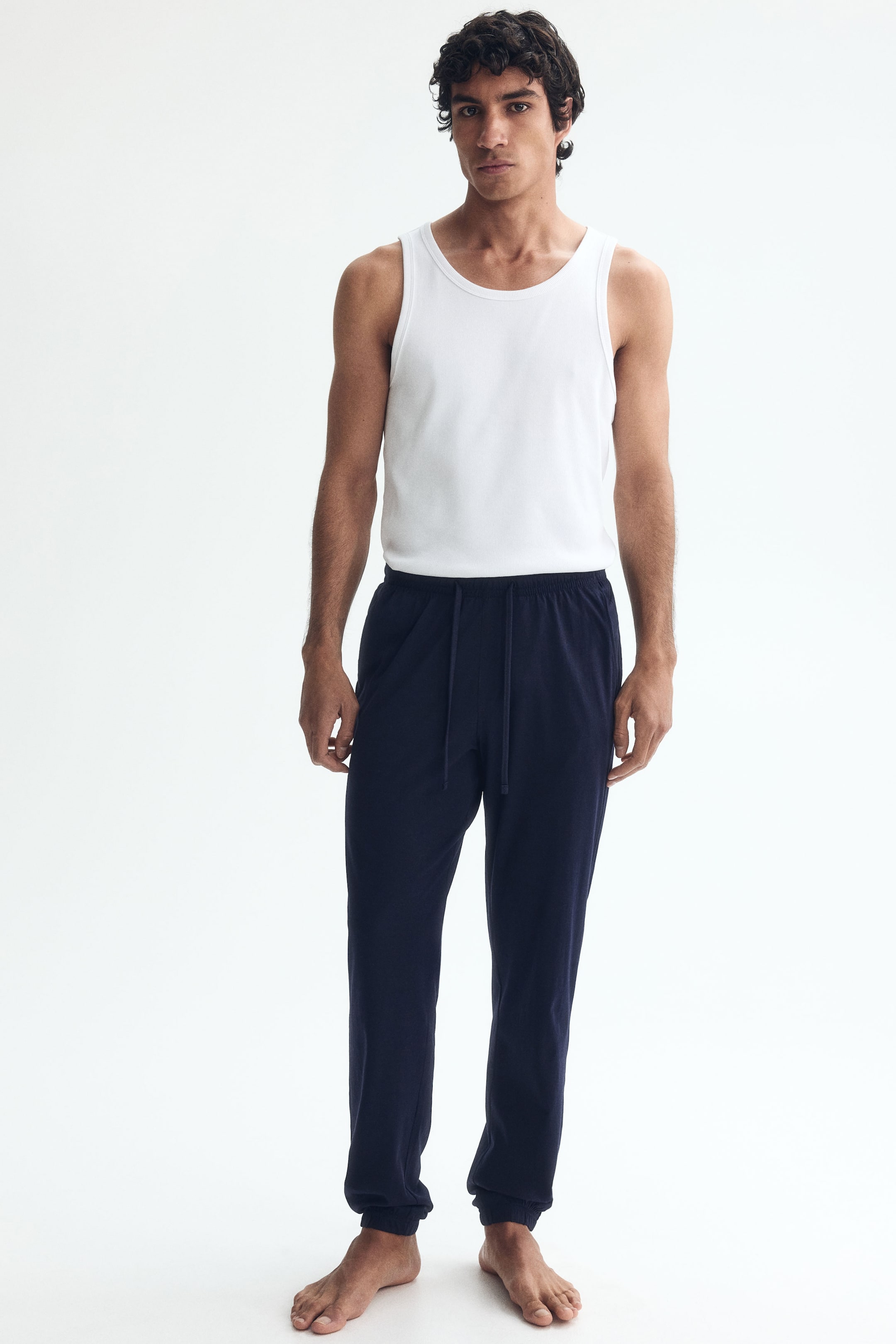 View larger image: Model is wearing dark blue cotton jersey sweatpants, featuring an elasticated drawstring waist, side pockets, and ribbed hems, offering a regular fit.