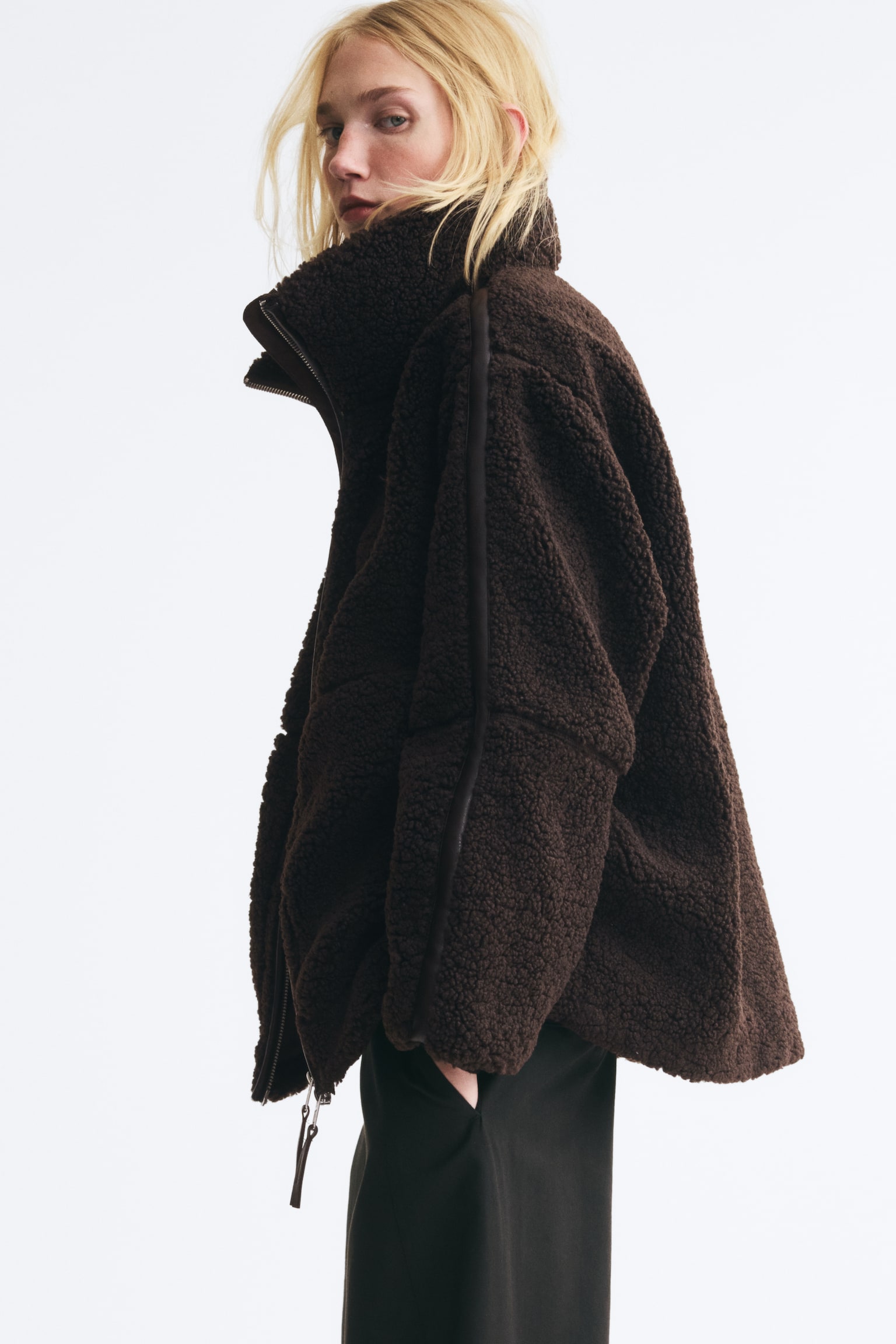 A dark brown bouclé fleece jacket is presenting its front, featuring a high stand-up collar and a full-length black zip. Darker trim is detailing the sides and sleeves, with two subtle front pockets visible. - 1