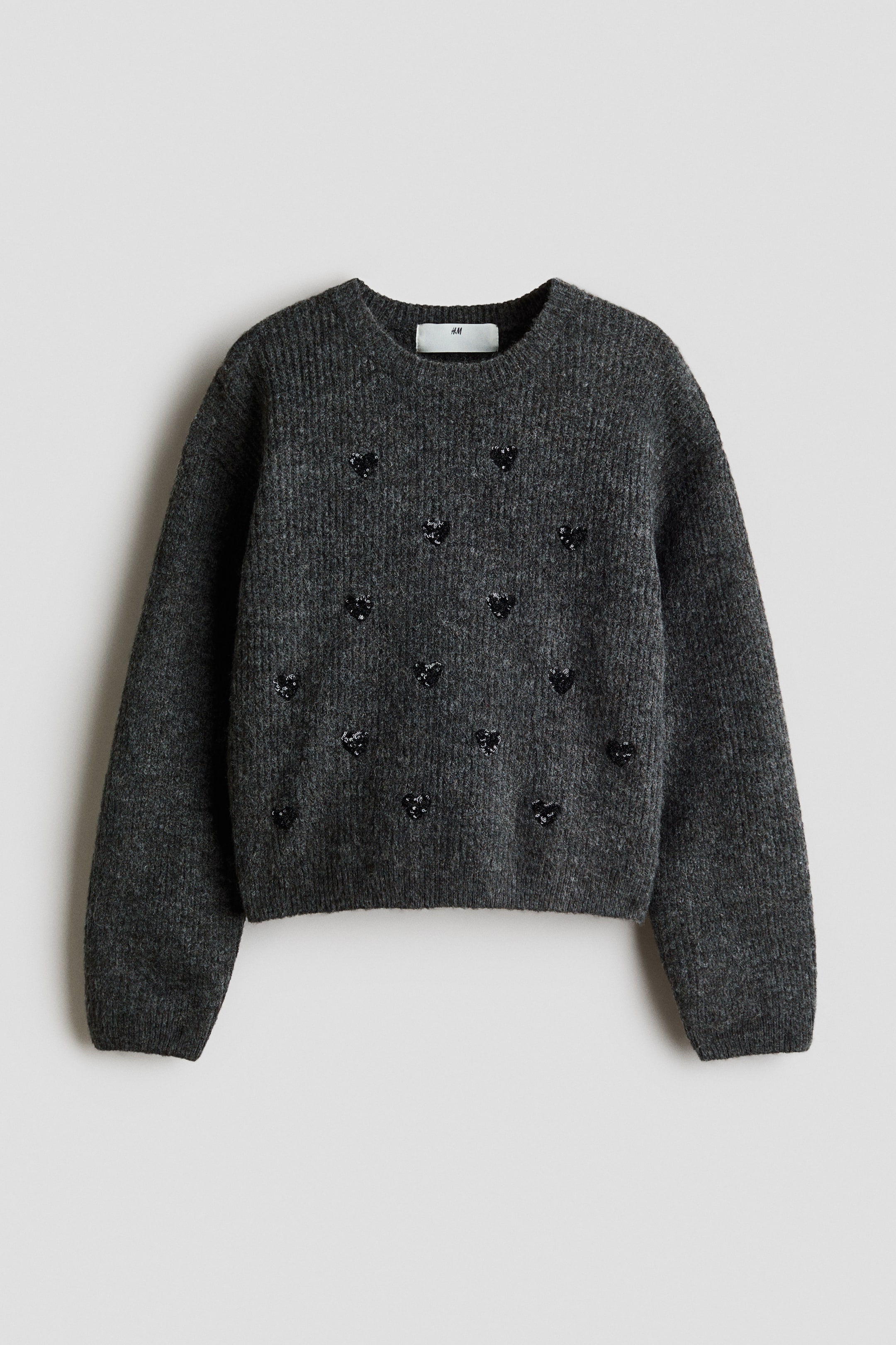 Ver imagen más grande: Un jersey gris oscuro con una textura de punto acanalado y lentejuelas negras en forma de corazón dispersas por el frente. Está diseñado con cuello redondo y puños y bajo acanalados.