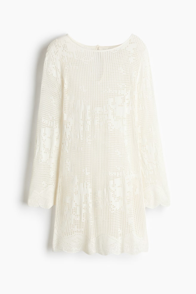 A cream crocheted tunic is showcasing its front, featuring a round neckline, long sleeves, and an intricate openwork pattern throughout. Scalloped hems complete the sleeves and the main body. - 1