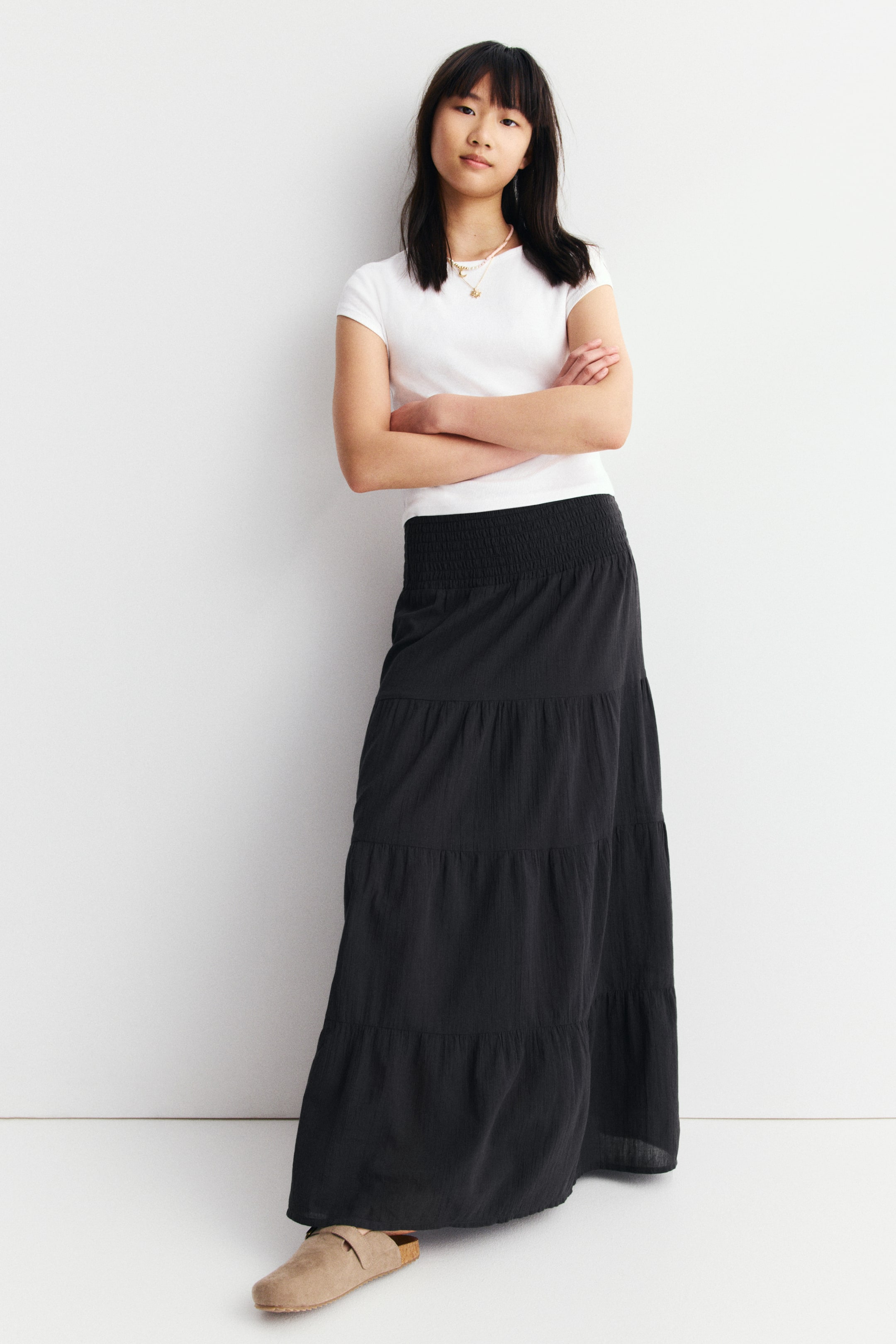 View larger image: A black crinkled tiered maxi skirt is featuring a prominent shirred waistband and three flowing tiers, presented from a front-right angle.