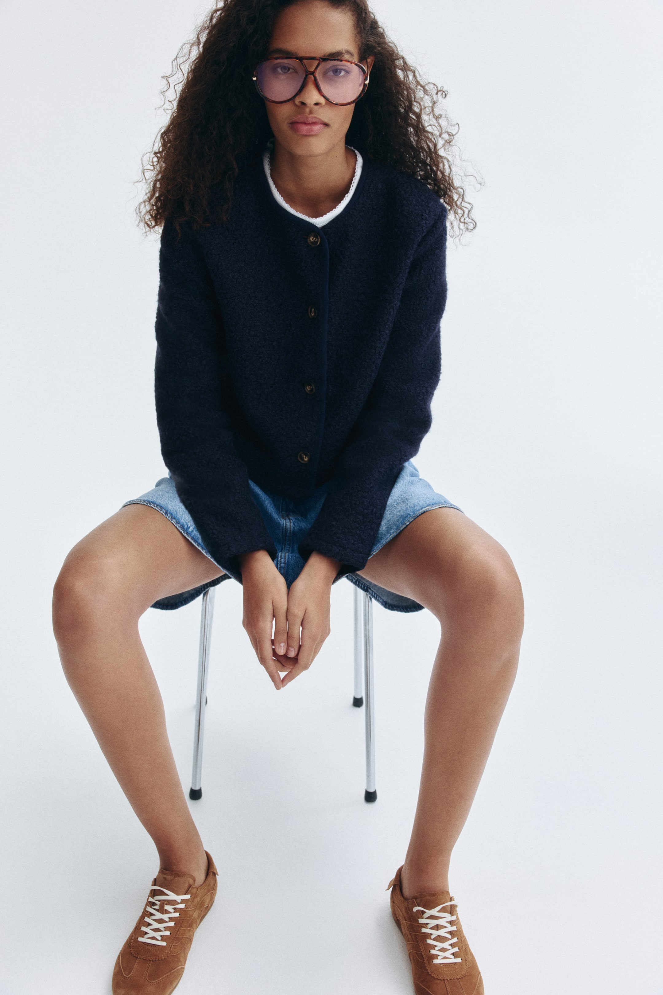 View larger image: A navy textured cardigan is being worn by the model. It features a round neckline with white trim and a front button closure, layered over a white top and styled with a denim skirt.