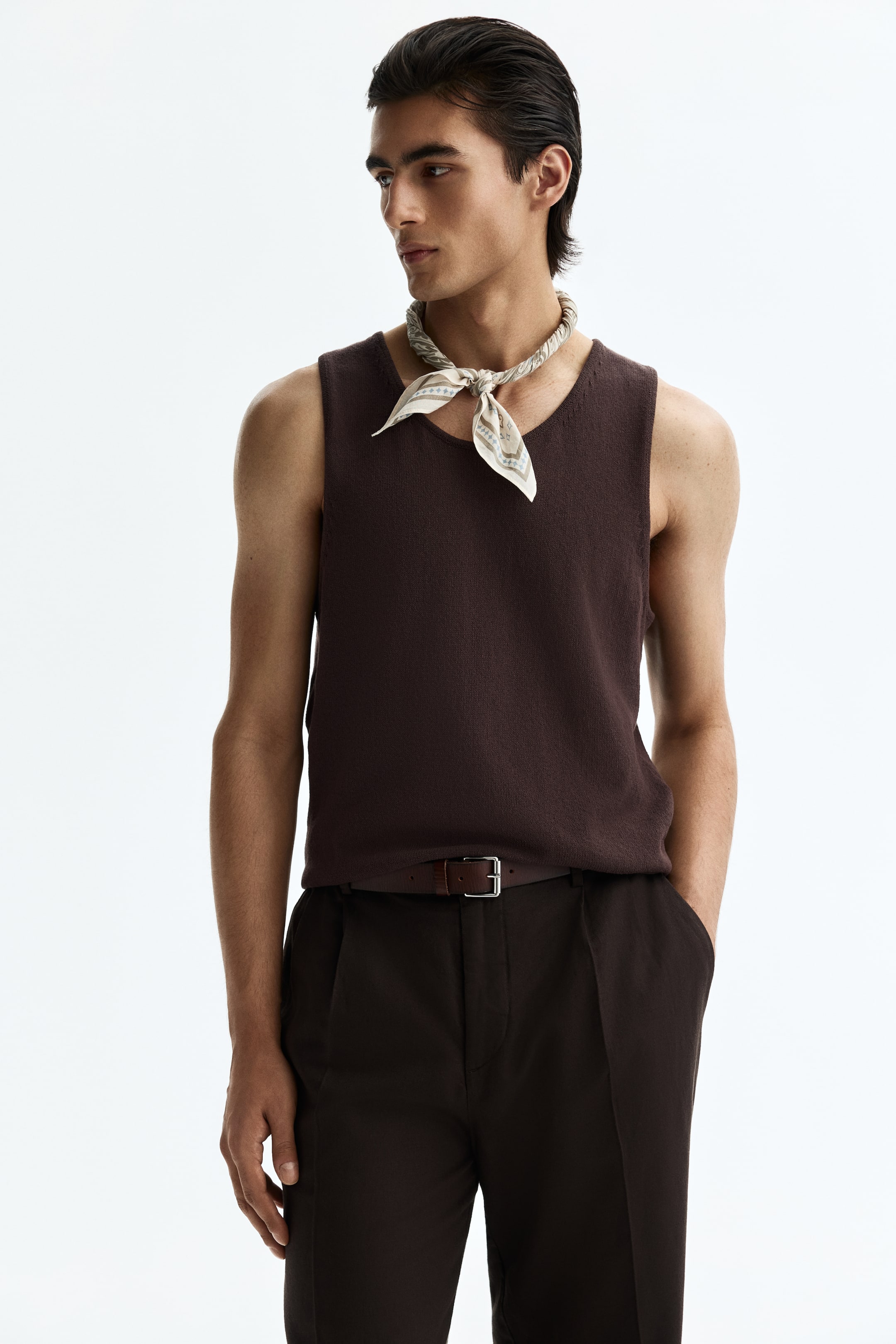 View larger image: A dark brown sleeveless top is shown facing forward, featuring a v-neckline and a textured knit fabric, tucked into dark brown pants with a patterned scarf around the neck.