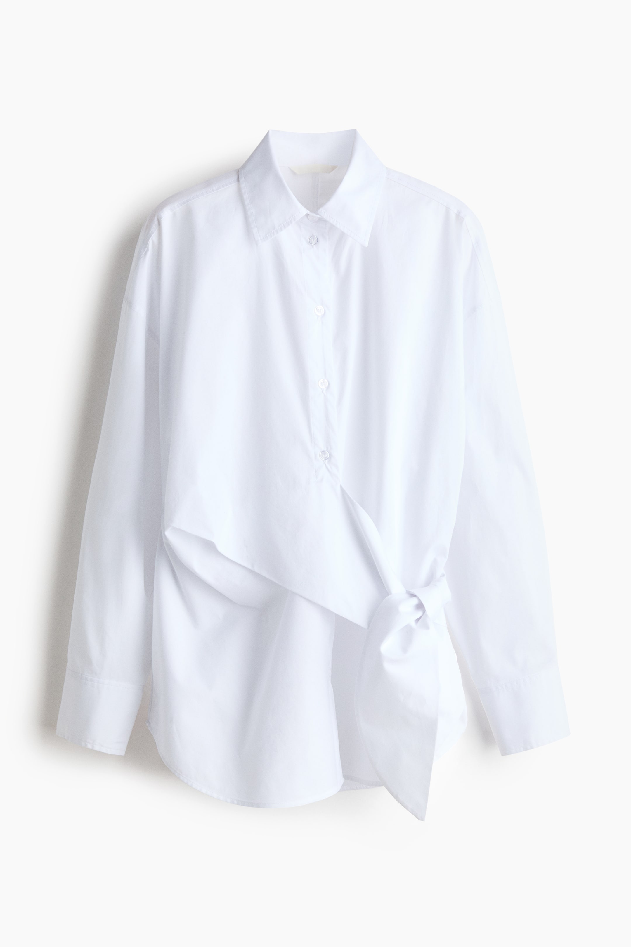 View larger image: A white long-sleeved shirt featuring a pointed collar and a front button placket, with a fabric panel wrapping from the left side and tying into a knot at the right hip.