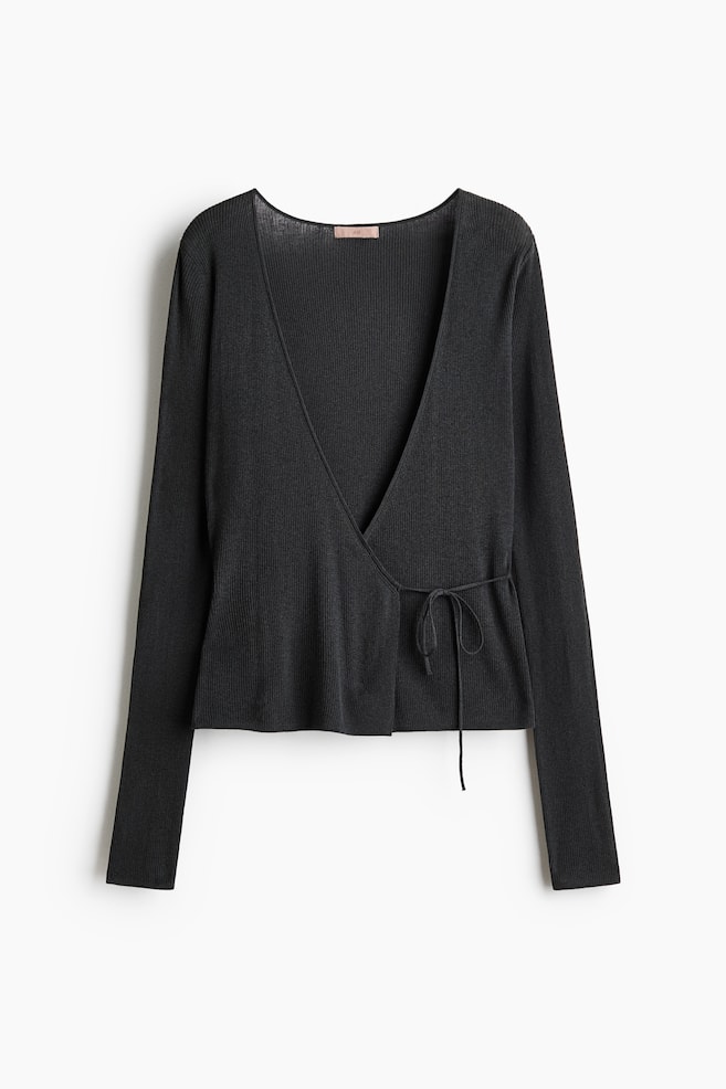 The black fitted cardigan is displayed facing forward, showcasing its soft, rib-knit cotton blend. It is featuring a deep V-neckline and a wrapover front, with narrow ties at the waist being knotted into a bow. - 1