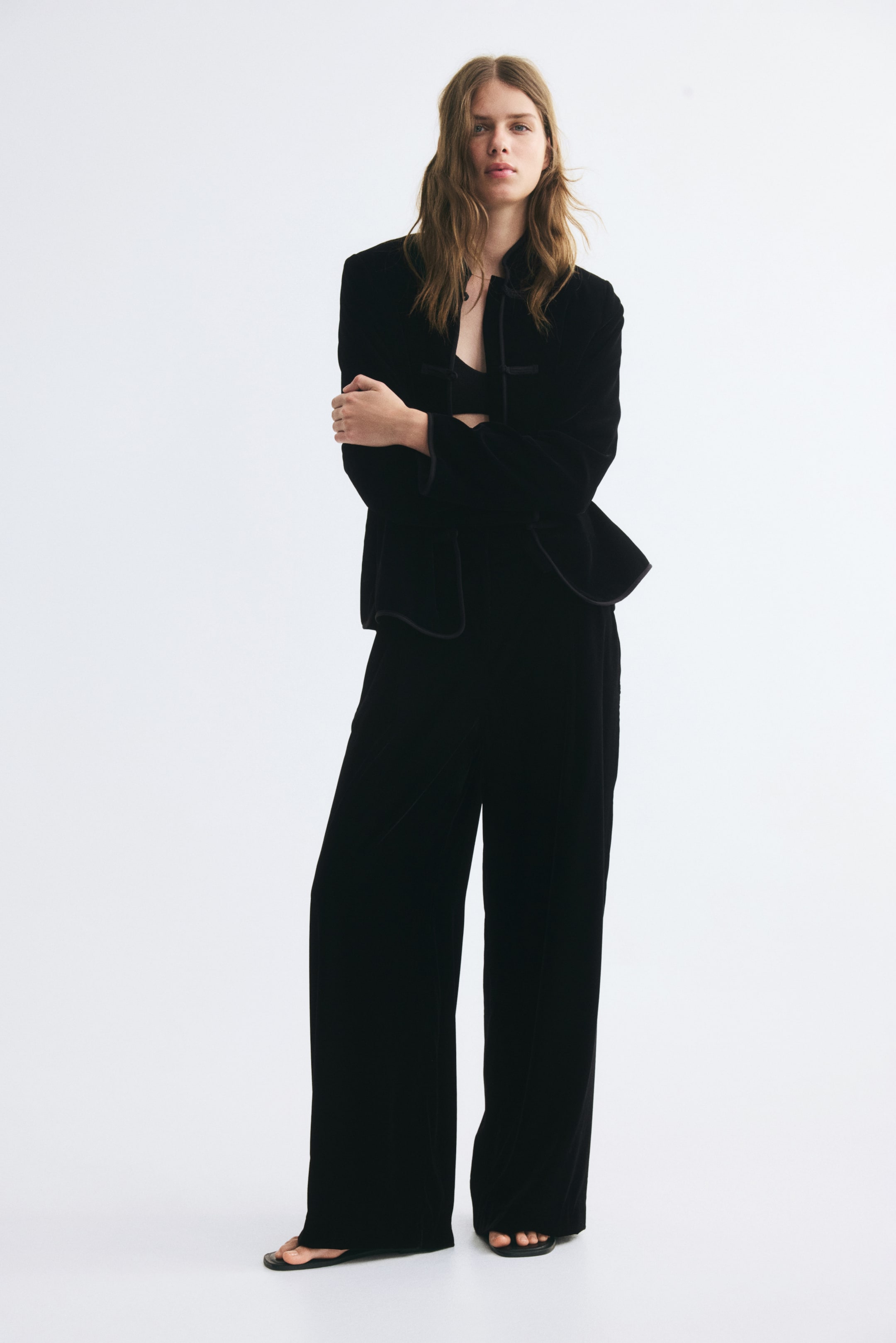 Voir une image plus grande: Le mannequin porte un pantalon noir à jambe large, agencé à une veste noire à manches longues assortie et à un haut court noir. Le pantalon présente une taille haute et une silhouette décontractée à jambe large qui tombe jusqu’au sol.