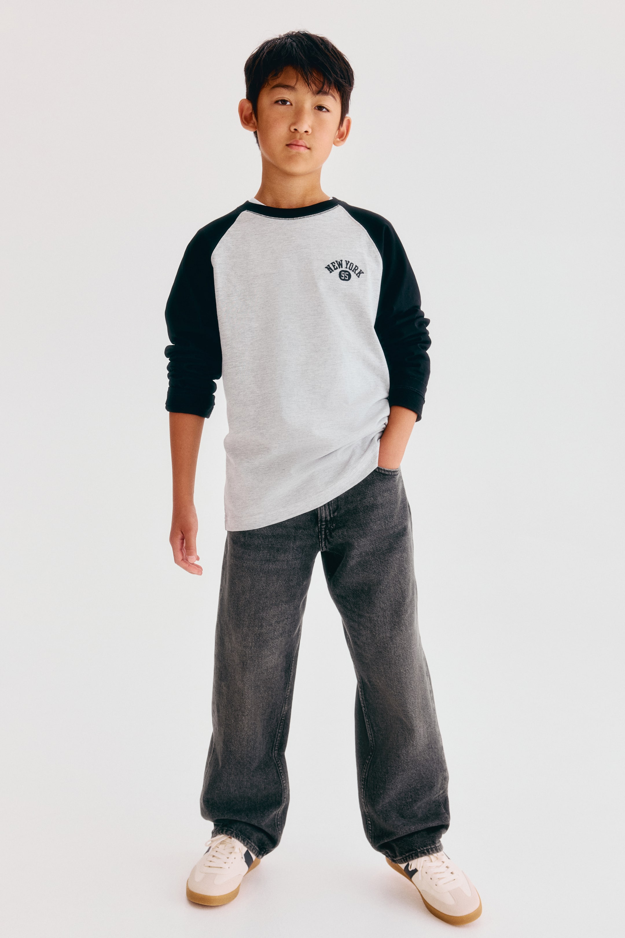 View larger image: These loose-fit, dark grey jeans in washed cotton denim are shown from the front, featuring a straight-leg silhouette that falls loosely over sneakers. The five-pocket design is styled with a long-sleeve T-shirt partially covering the waistband.