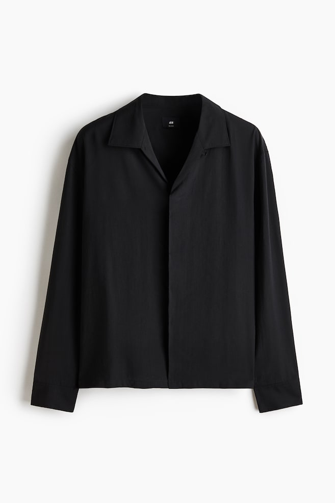 A black long-sleeved shirt is laid flat, showcasing its front side. It features an open revere collar forming a V-neckline, and long sleeves with simple cuffs. - 1