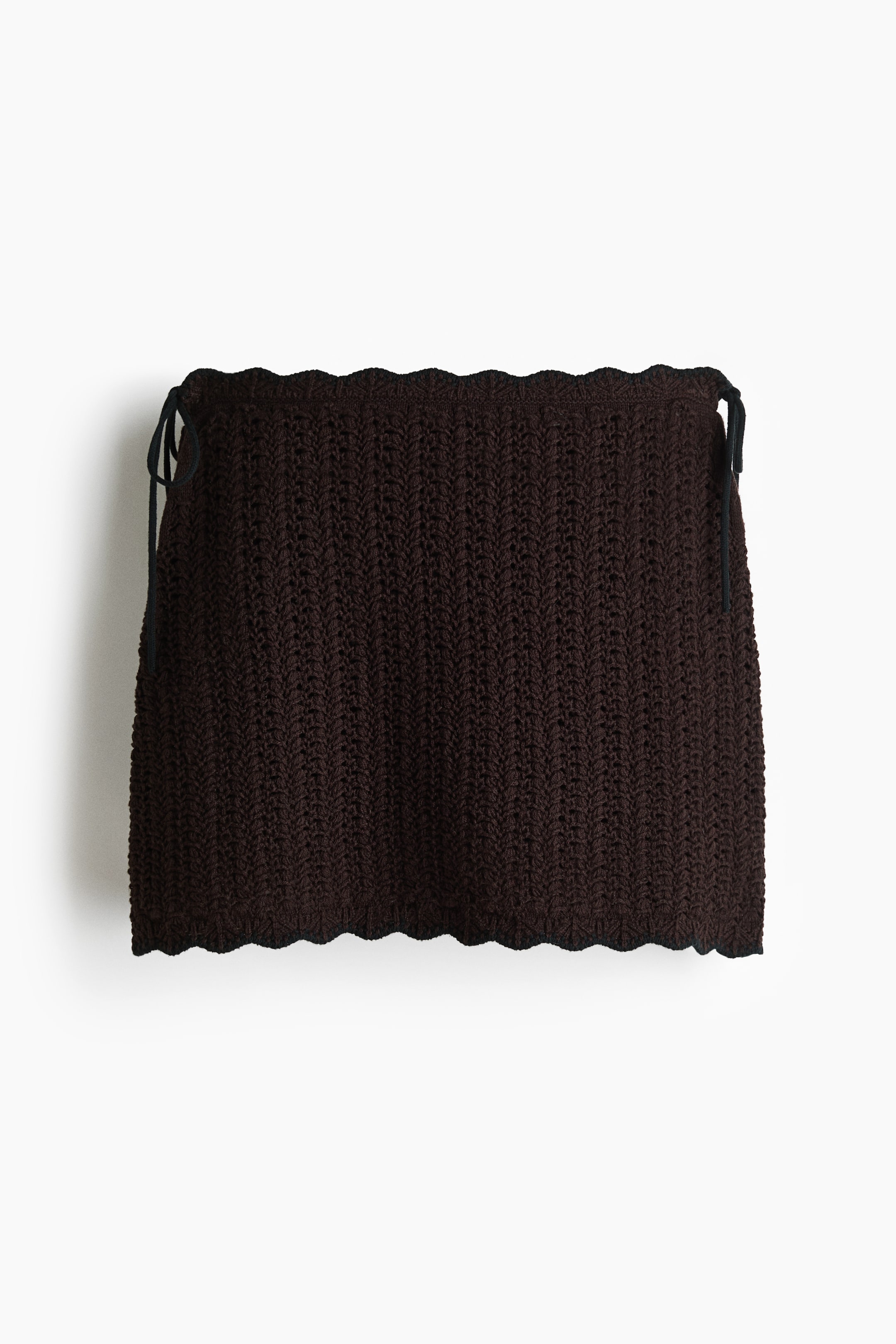 Visualizza immagine più grande: Una minigonna in crochet marrone scuro, presentata FRONT, caratterizzata da un motivo a punto verticale, bordi superiori e inferiori smerlati e lacci neri su entrambi i lati superiori.