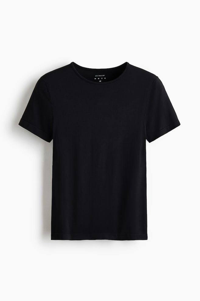 The Seamless Slim Fit Sports top with SoftMove? is presented front-facing, featuring a black, smooth fabric, short sleeves, and a rounded neckline. A small white label displaying 'DRYMOVE' and 'H&M' is visible on the inside back of the neck. - 1