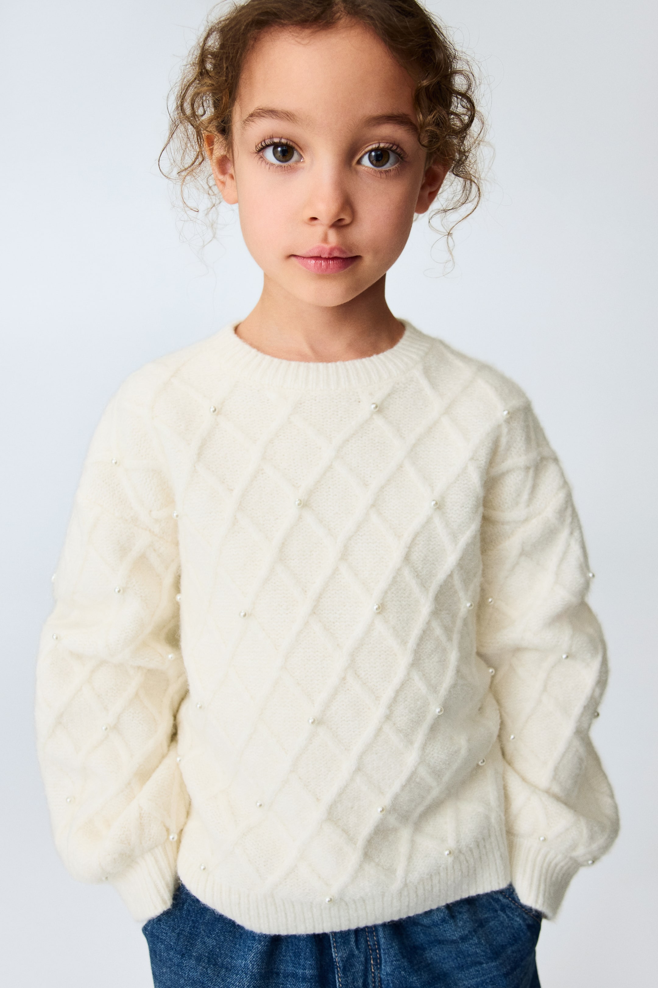 View larger image: An off-white jumper showcases a textured diamond knit pattern embellished with small pearl-like beads at each intersection. It features a ribbed round neck, long sleeves with ribbed cuffs, and a ribbed hem, offering a relaxed fit from the front.
