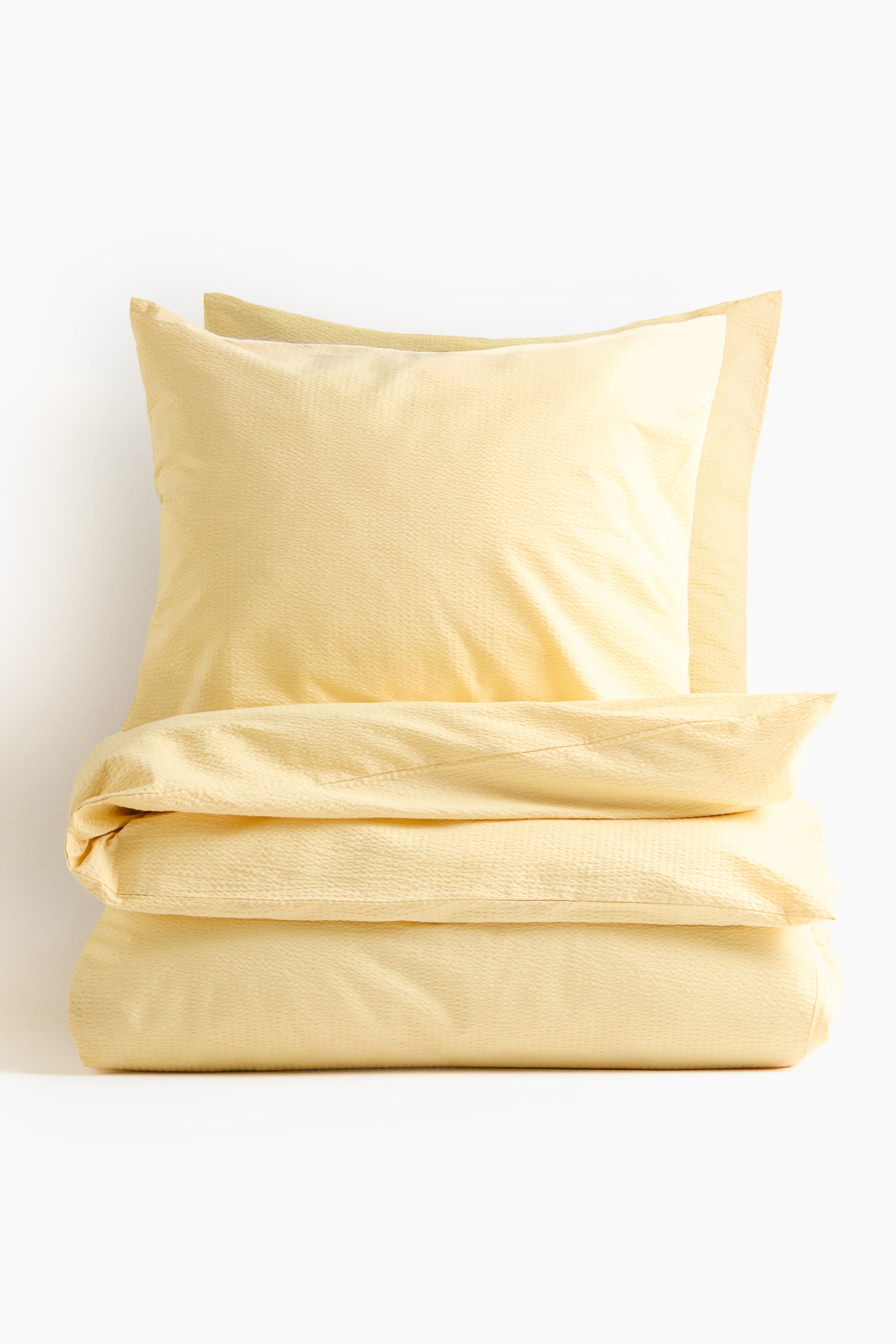 View larger image: A light yellow seersucker duvet cover set is shown, presented from the front. The duvet cover is neatly folded horizontally, and a plump pillowcase is resting on top, both displaying the characteristic puckered seersucker texture.