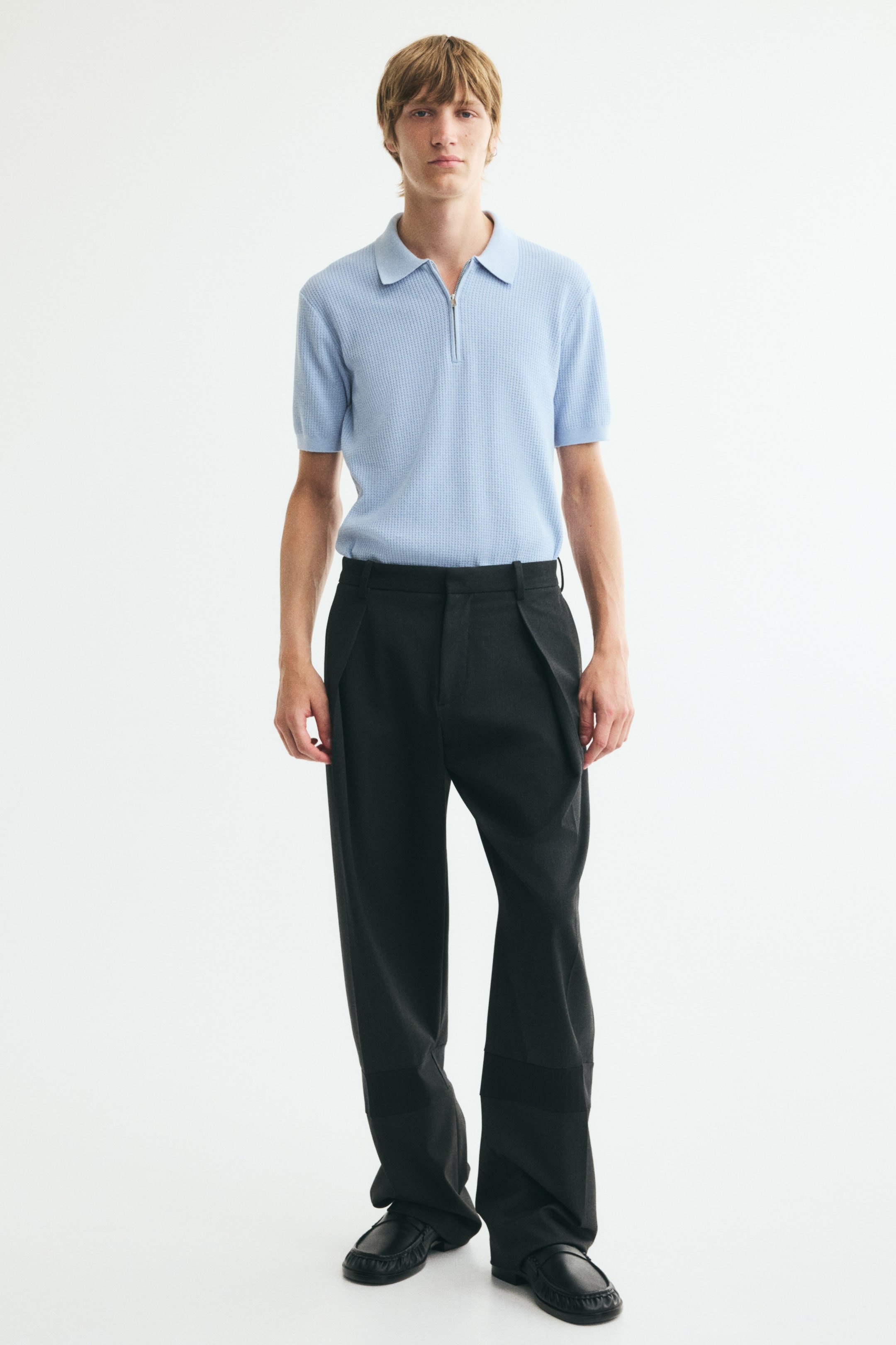 View larger image: A light blue, textured-knit polo shirt is being worn by the model, tucked into wide-leg black trousers. The slim-fit shirt features a ribbed collar with a partially open half-zip fastening and short sleeves with ribbed cuffs.