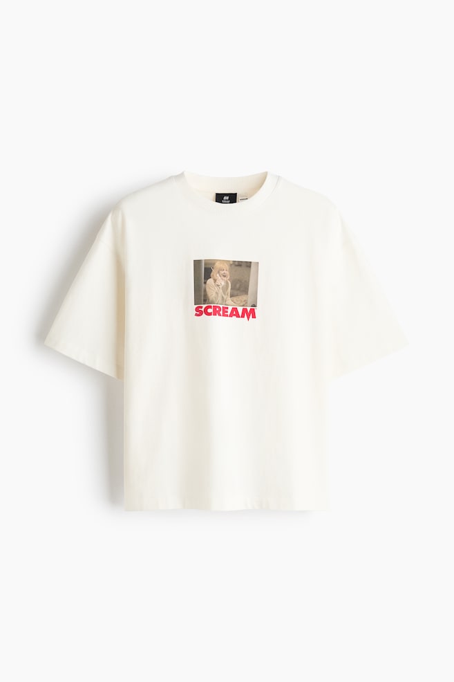 Een off-white T-shirt met relaxed fit is van voren afgebeeld, met een geribde ronde hals en wijde korte mouwen. Op de borst staat een kleine rechthoekige grafische print van een filmscÃ¨ne, met direct daaronder het woord "SCREAM" in opvallende rode letters. - 1