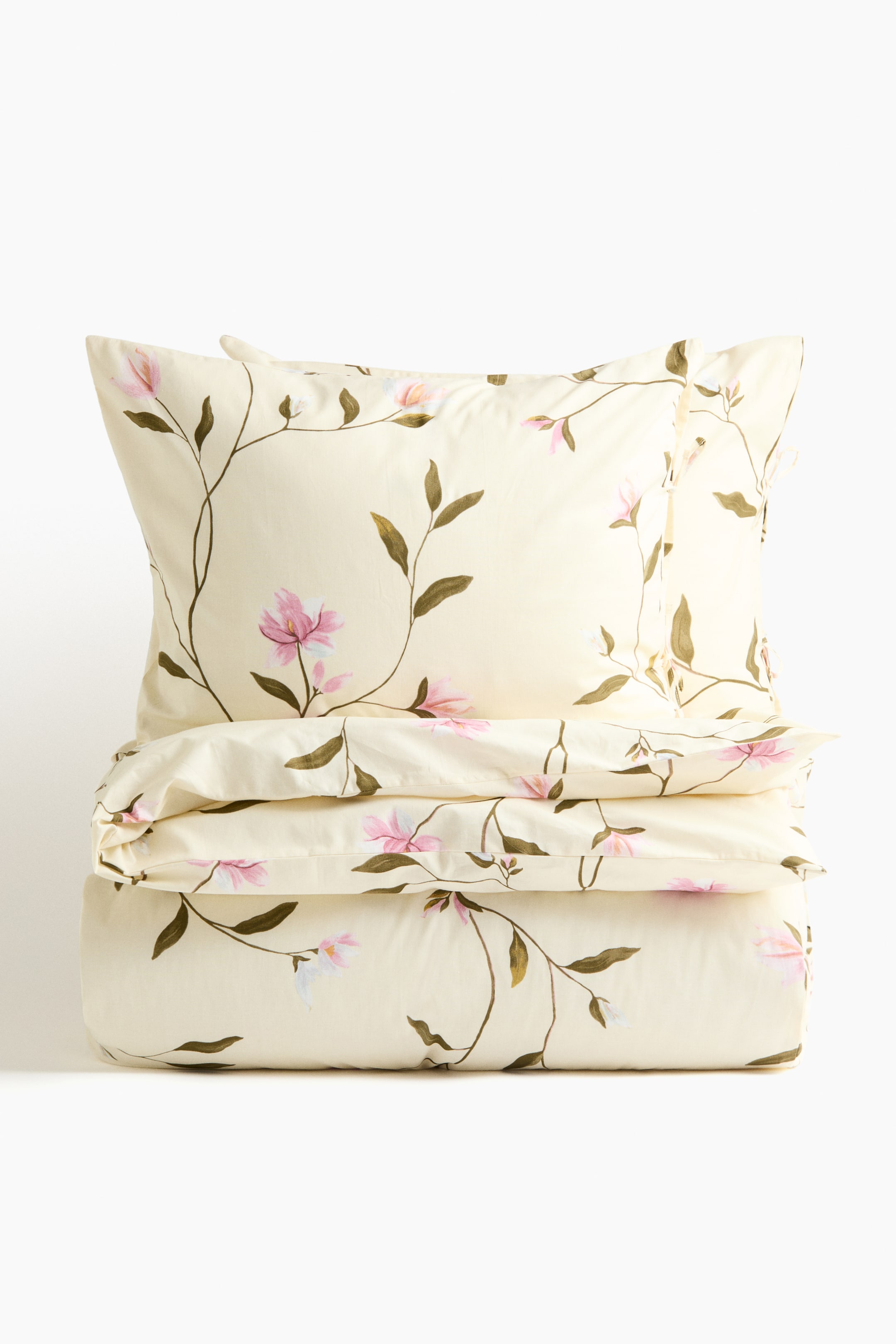 View larger image: A pale yellow duvet cover set is featuring a vining floral pattern with pink and white blossoms and green leaves. A pillowcase is resting on top of the folded duvet cover, both displaying the pattern.