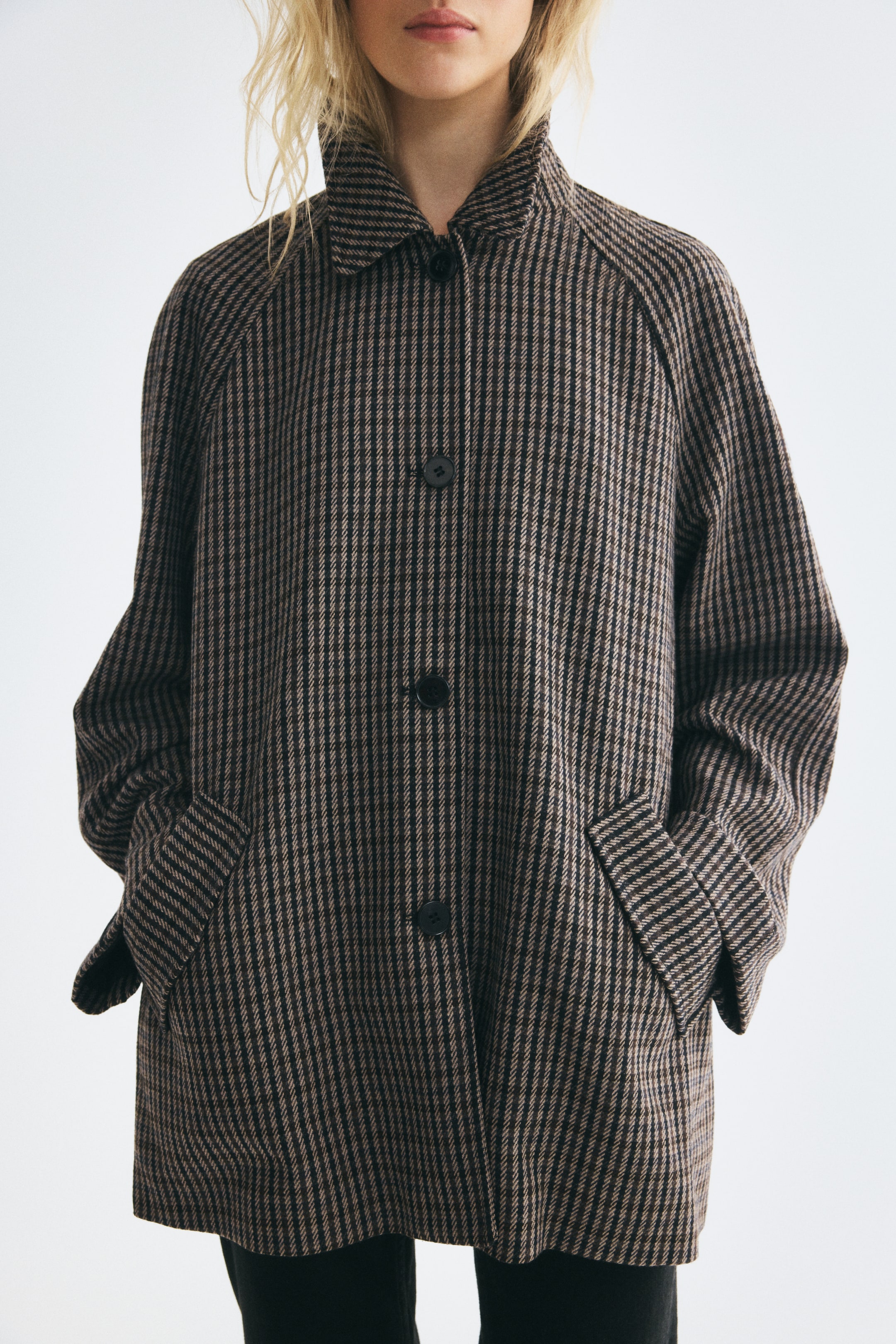 View larger image: A woven car coat with a brown and black striped pattern is shown from the front, featuring a pointed collar, a button-down front, and raglan sleeves. The coat is worn with hands resting in the angled front flap pockets, highlighting its relaxed fit.