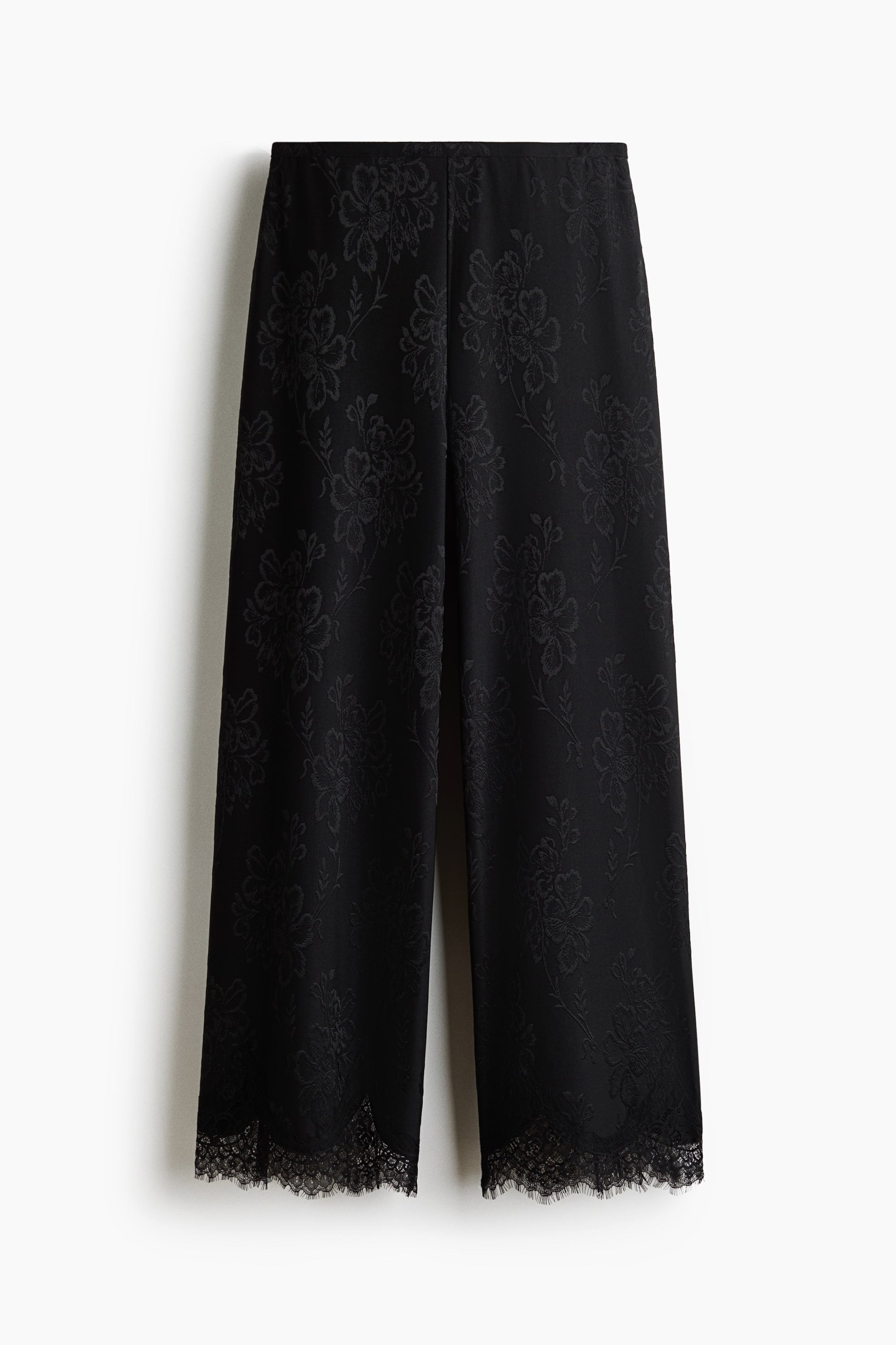 Voir une image plus grande: Une paire de pantalons noirs coupe décontractée en jersey jacquard floral est suspendue de face, mettant en valeur une taille haute et des jambes larges. Les jambes tombent droit et se terminent par une délicate finition en dentelle noire festonnée à l’ourlet.