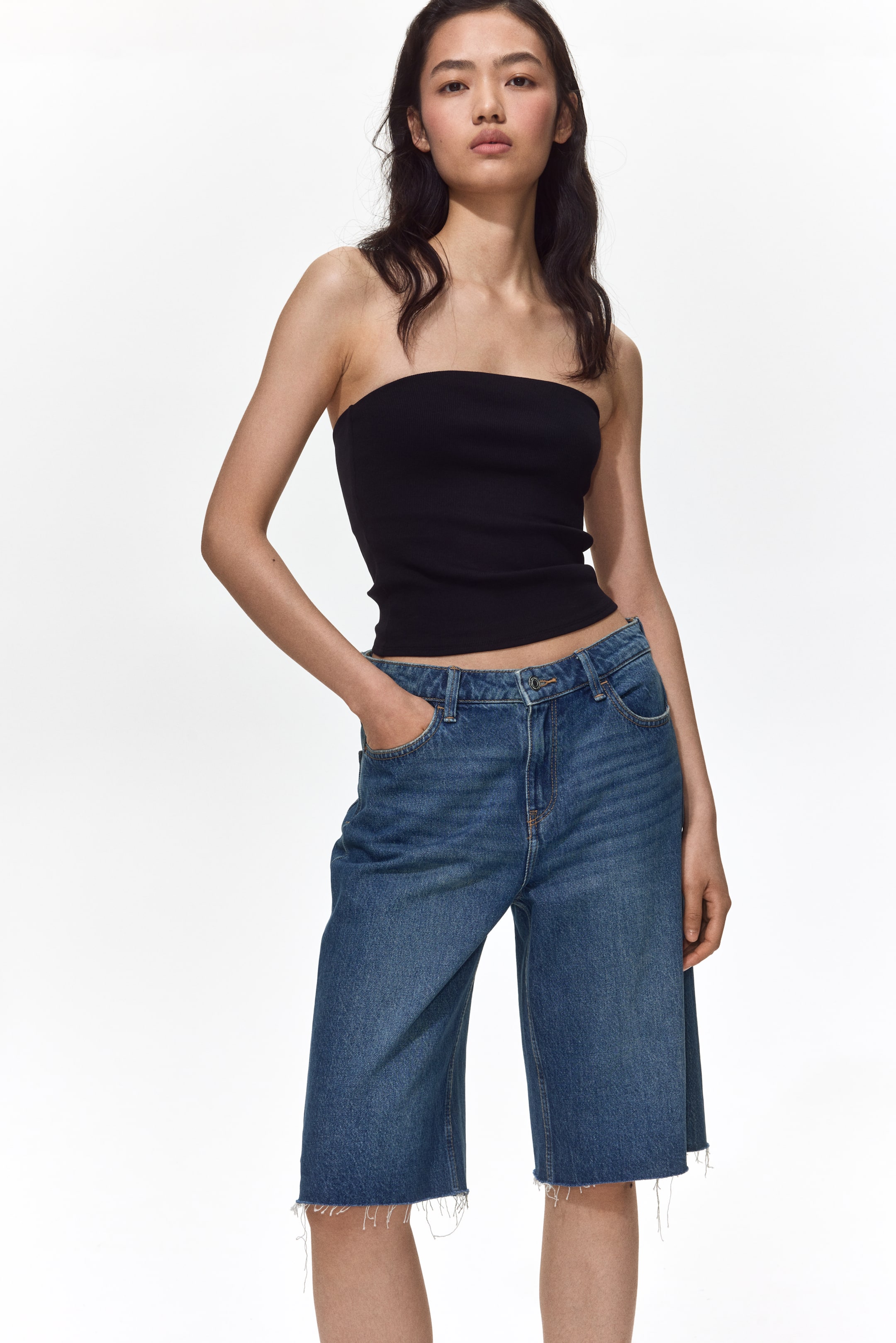 View larger image: A black ribbed tube top is paired with blue denim Bermuda shorts, featuring a five-pocket design, a relaxed fit, and frayed hems.