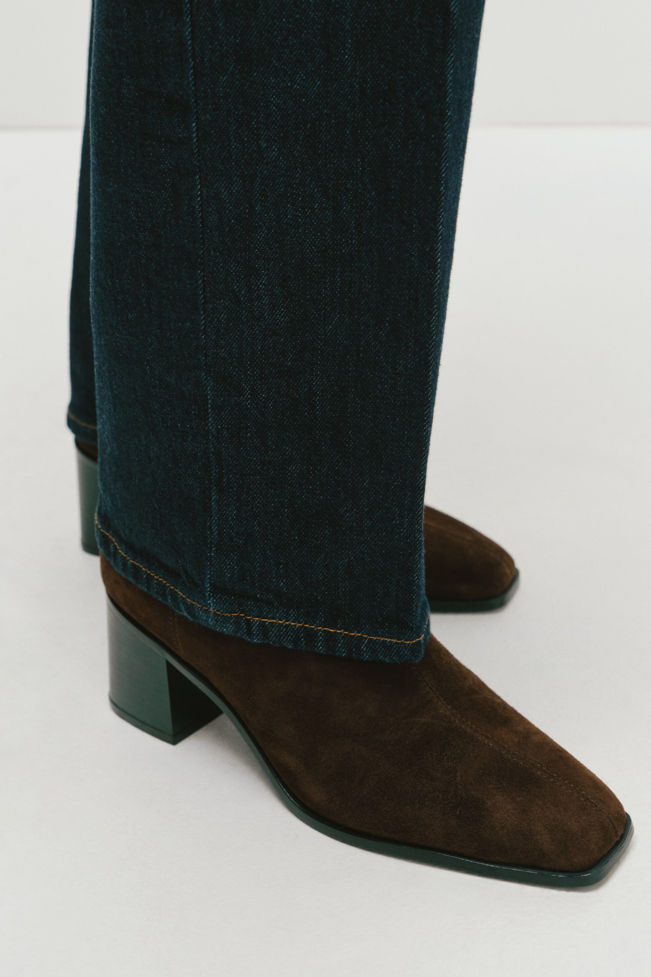 Voir une image plus grande: Des bottines en suède brun à bout carré et à talon bloc sont portées par le mannequin sous un jean droit bleu foncé.