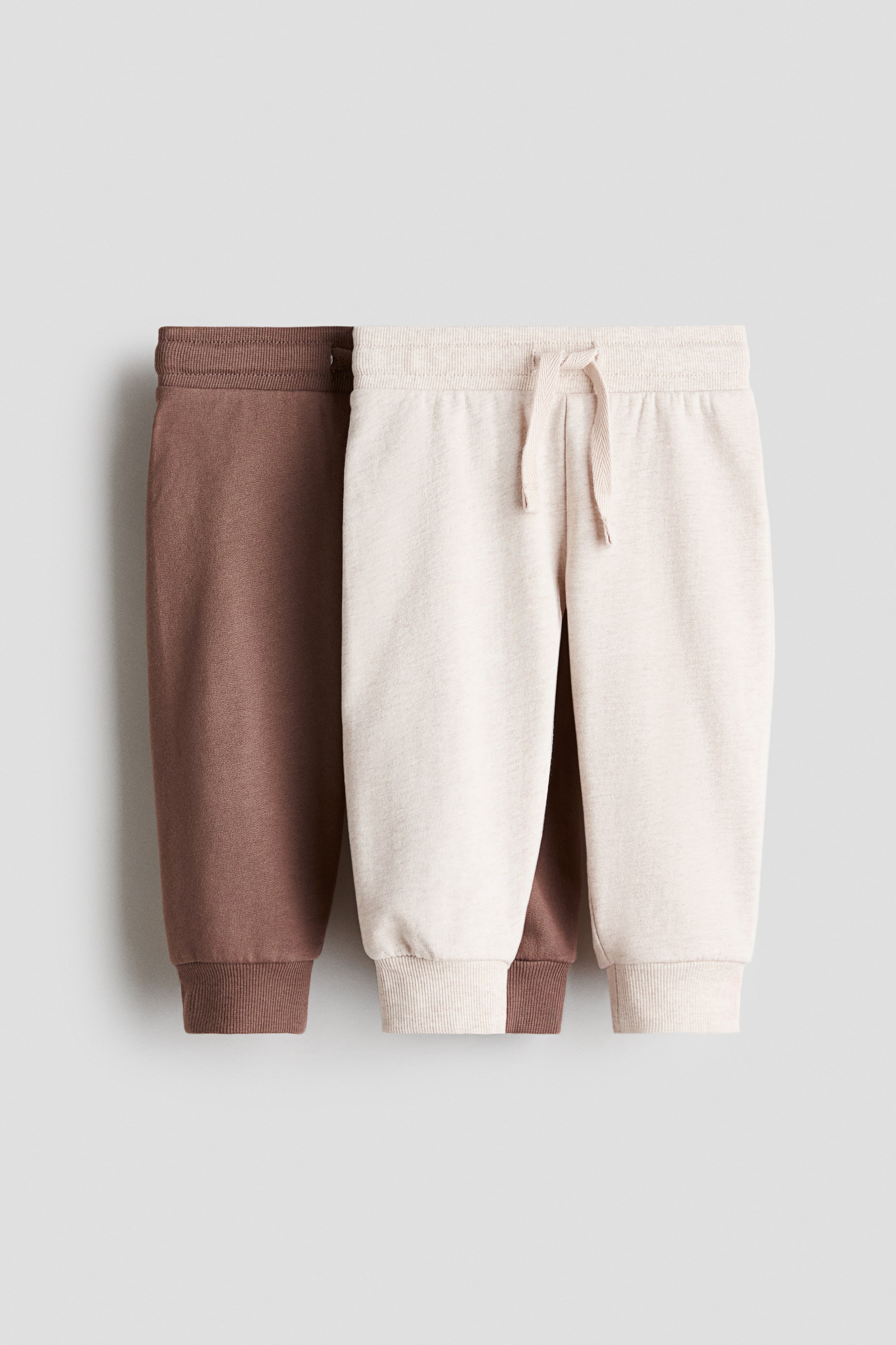 View larger image: Joggers are showcased in two pairs, one in light beige and the other in brown, both facing forward. They feature an elasticated drawstring waist, ribbed hems, and a soft sweatshirt fabric.