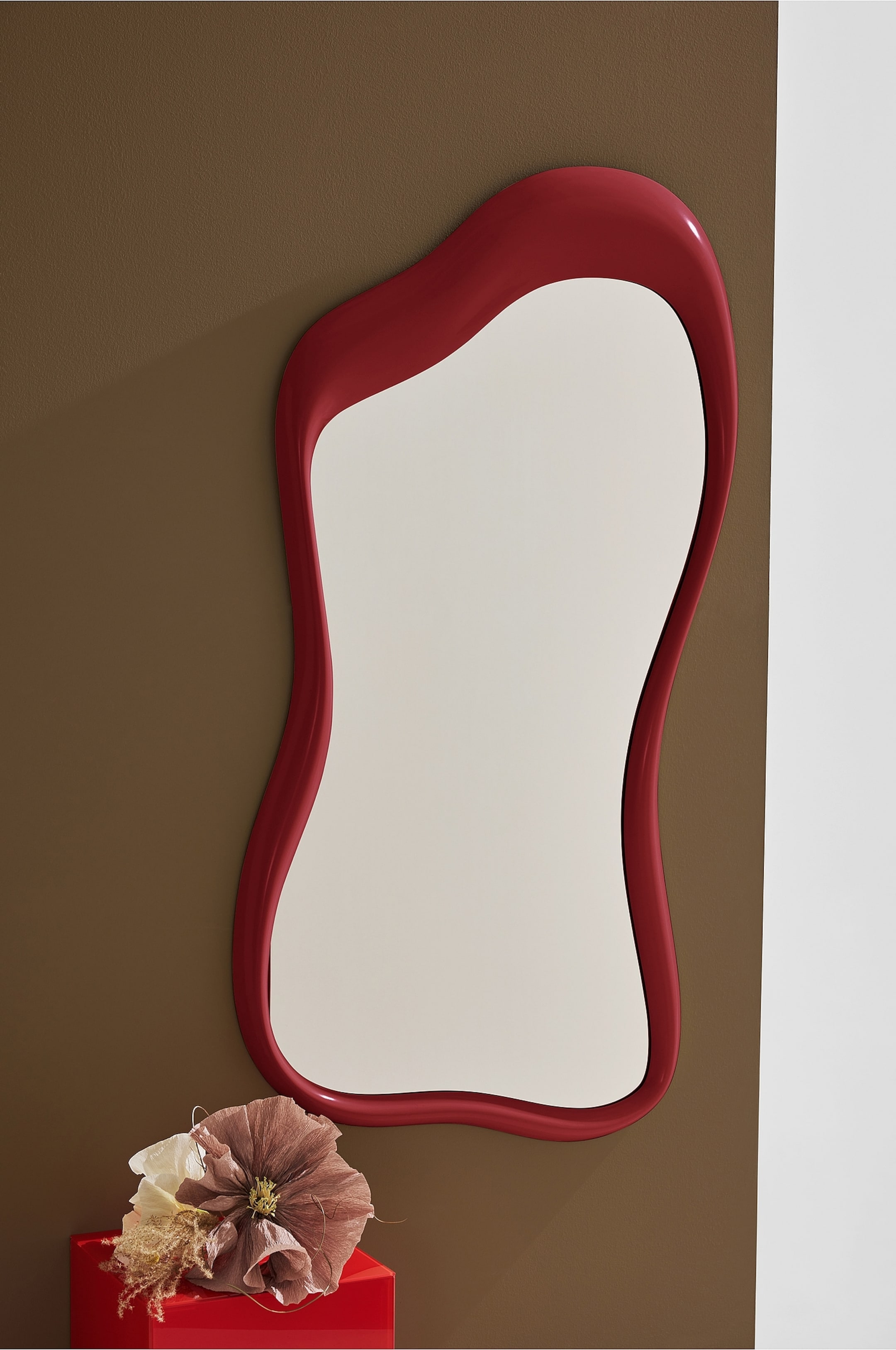 Agrandir l'image: Un miroir présente une silhouette irrégulière et ondulée, avec un cadre épais et brillant de couleur rouge qui souligne sa forme.