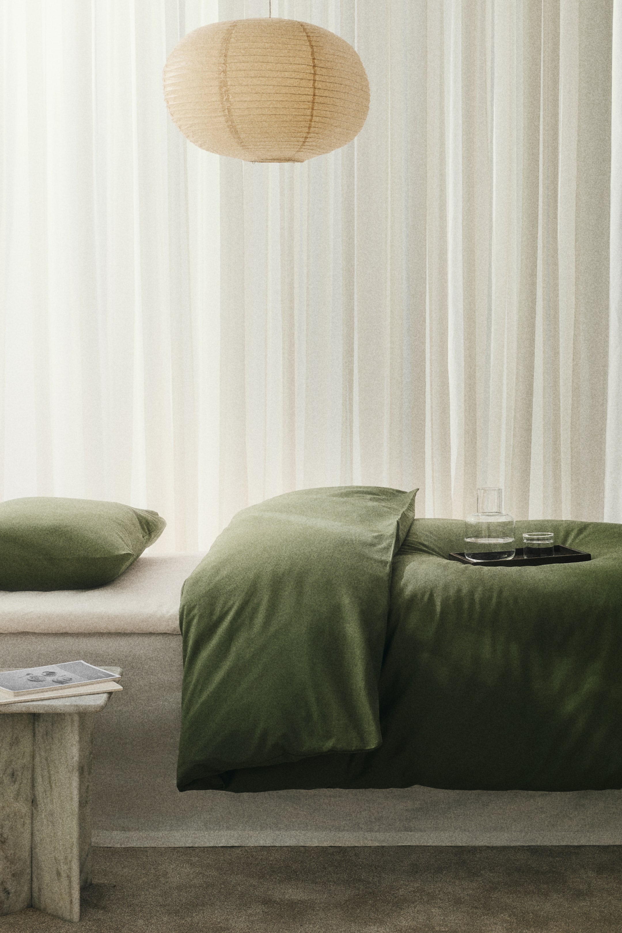 이미지 확대 보기: 어두운 녹색의 부드러운 질감의 침구 세트가 전시되어 있으며, 이불 커버가 드레이프되어 있고 매칭되는 베개가 밝은 색상의 쿠션 위에 놓여 있습니다. 투명한 유리 물병과 컵을 담고 있는 검은색 쟁반이 드레이프된 이불 위에 놓여 있습니다.