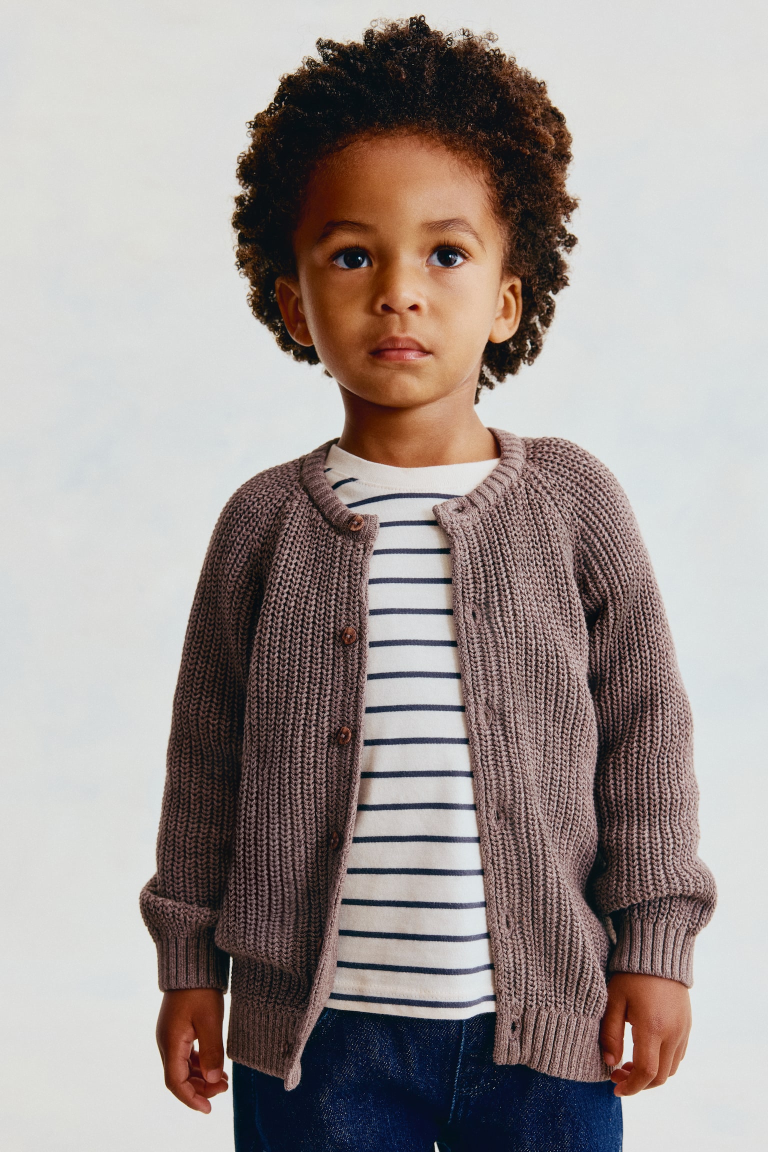 Ce cardigan en coton tricotÃ© Ã  motif patent, dans une teinte taupe attÃ©nuÃ©e, est prÃ©sentÃ© de face, portÃ© ouvert par-dessus un t-shirt rayÃ©. Le cardigan prÃ©sente un col rond bordÃ© de cÃ´tes, de longues manches raglan avec poignets cÃ´telÃ©s, ainsi que des boutons bruns le long de lâouverture devant. - 1