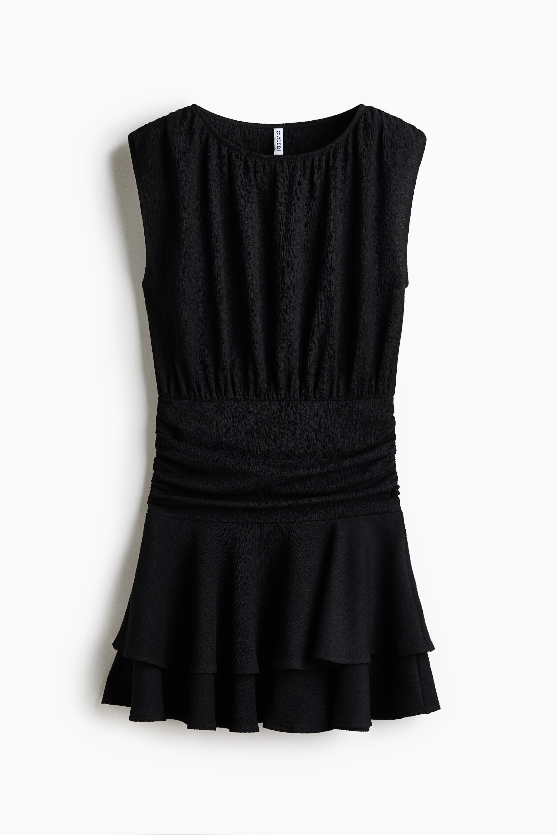 View larger image: The black dress showcases its front, highlighting a round neckline, sleeveless style, and textured fabric throughout. The bodice gathers at the neckline and cinches at the waist with ruched detailing, while the skirt flares out with two layered ruffles.
