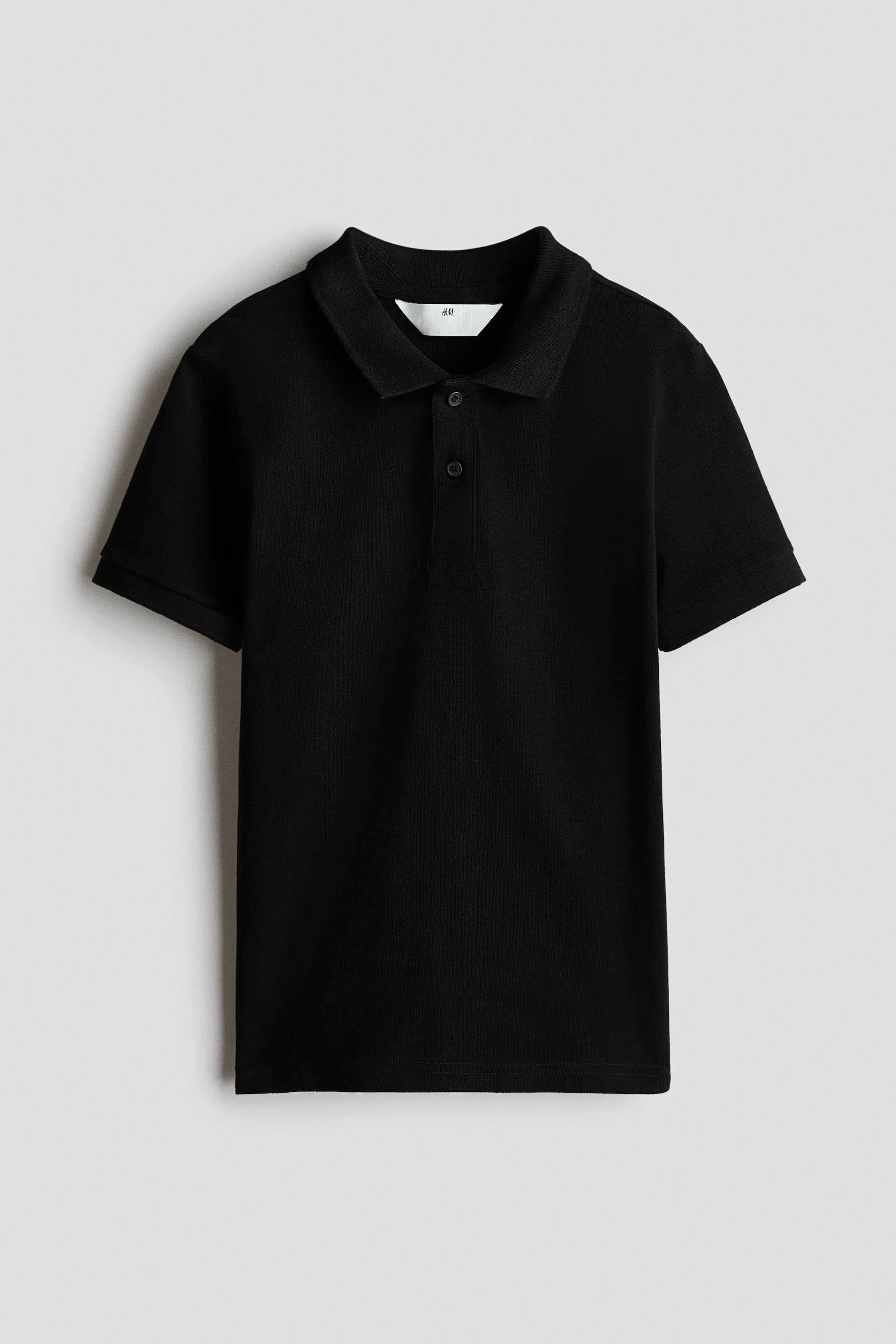 View larger image: A black polo shirt is facing front, featuring a pointed collar, a two-button placket with black buttons, and short sleeves with ribbed cuffs. A white H&M label is visible at the back of the neck.