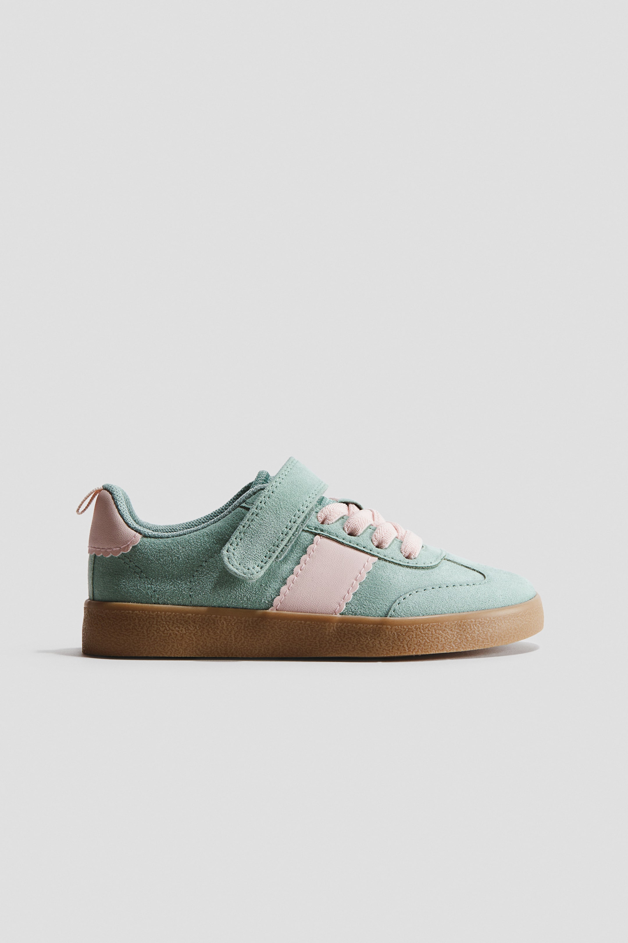 View larger image: Trainer. This trainer features a mint green suede-like upper accented with light pink details, including a scalloped-edge side stripe and matching scalloped trim on the collar, complemented by pink laces. A hook-and-loop strap secures over the laces, while a flat brown rubber sole completes the design.