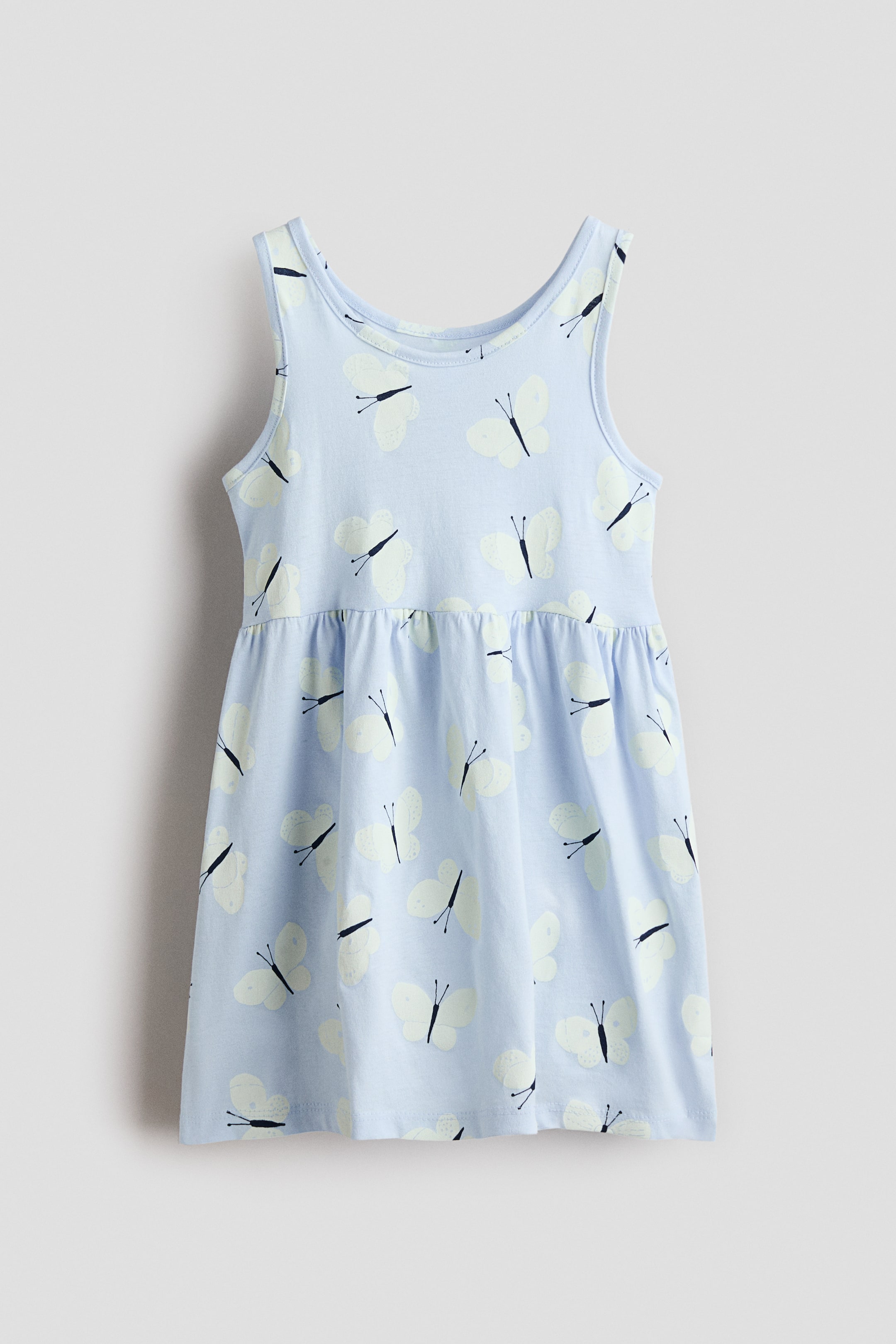View larger image: A sleeveless dress is presented from the FRONT, featuring a light blue cotton jersey fabric with a white butterfly pattern. It is designed with a gathered seam at the waist and a gently flared skirt.