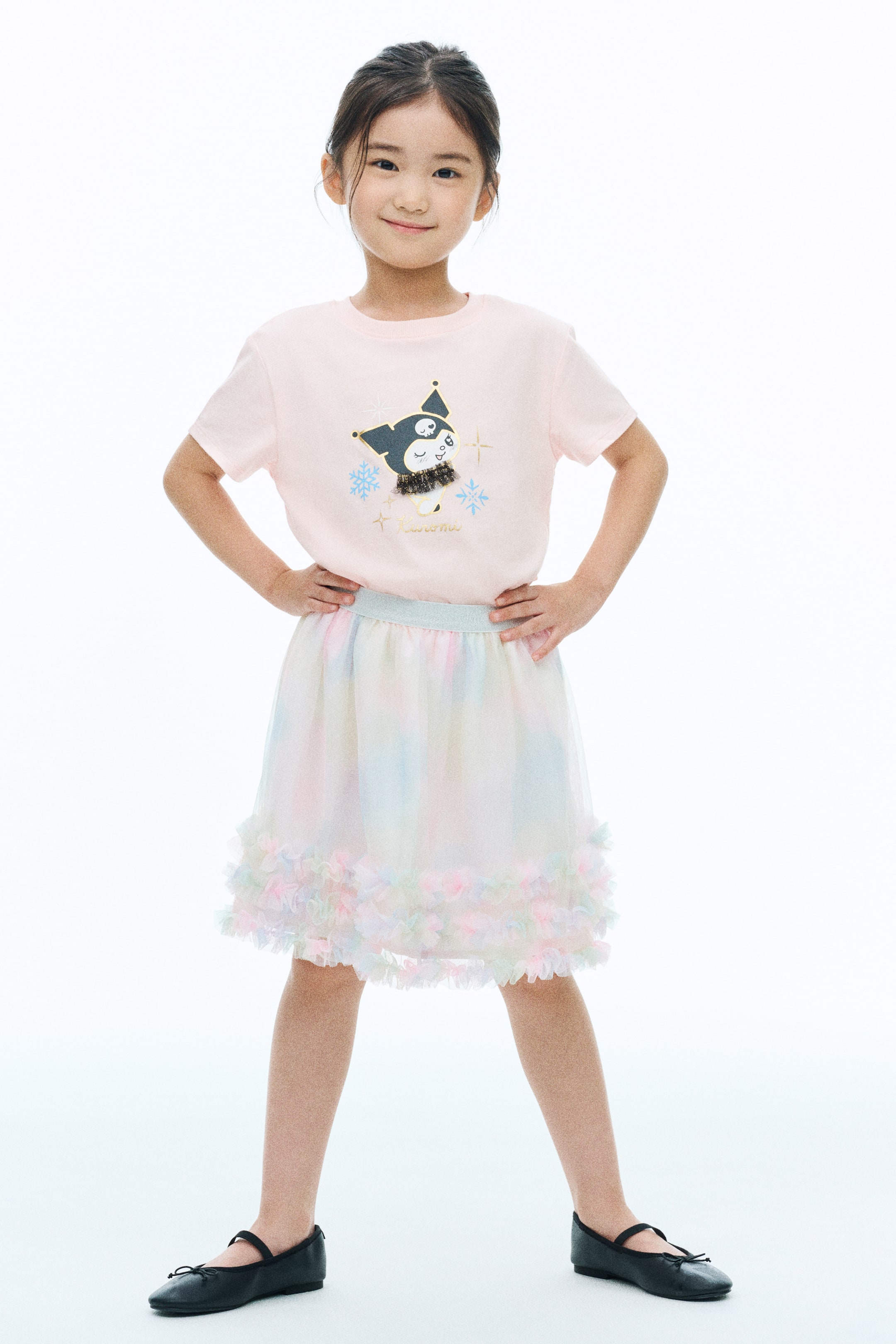 View larger image: A light pink, short-sleeved T-shirt featuring a central cartoon character motif with snowflake details and a small tulle embellishment is being worn by the model. The T-shirt is tucked into a pastel, multi-colored tulle skirt.