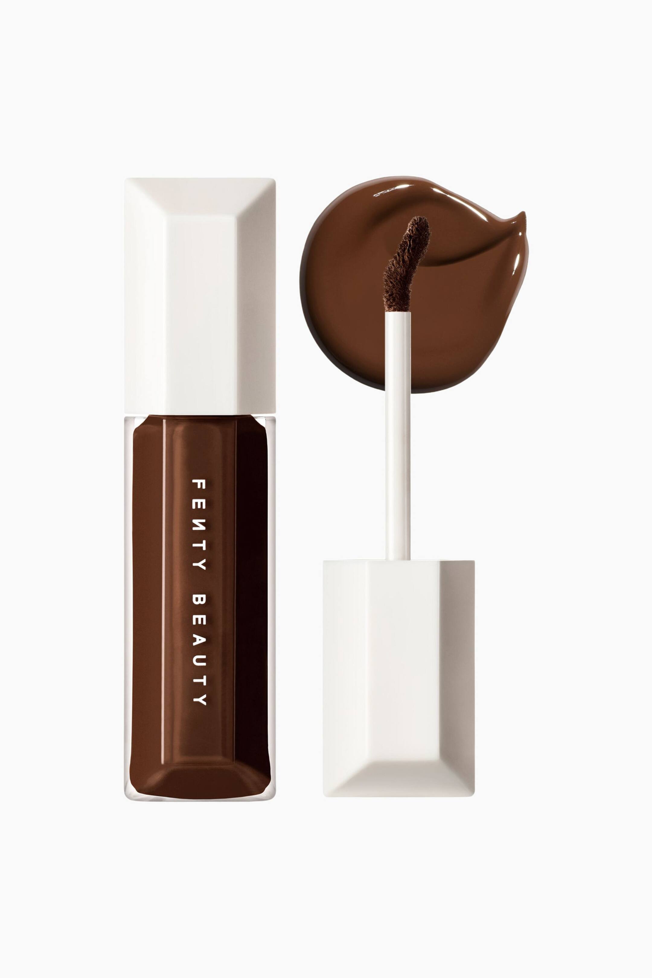 Visa större bild: We're Even Hydrating Longwear Concealer står upprätt i en genomskinlig, facetterad rektangulär flaska med vitt lock och visar en djupbrun nyans inuti. Bredvid flaskan står applikatorstaven vertikalt med sin böjda, vinklade doe-foot-spets riktad uppåt framför en glansig, cirkelformad swatch av den matchande mörkbruna concealern.